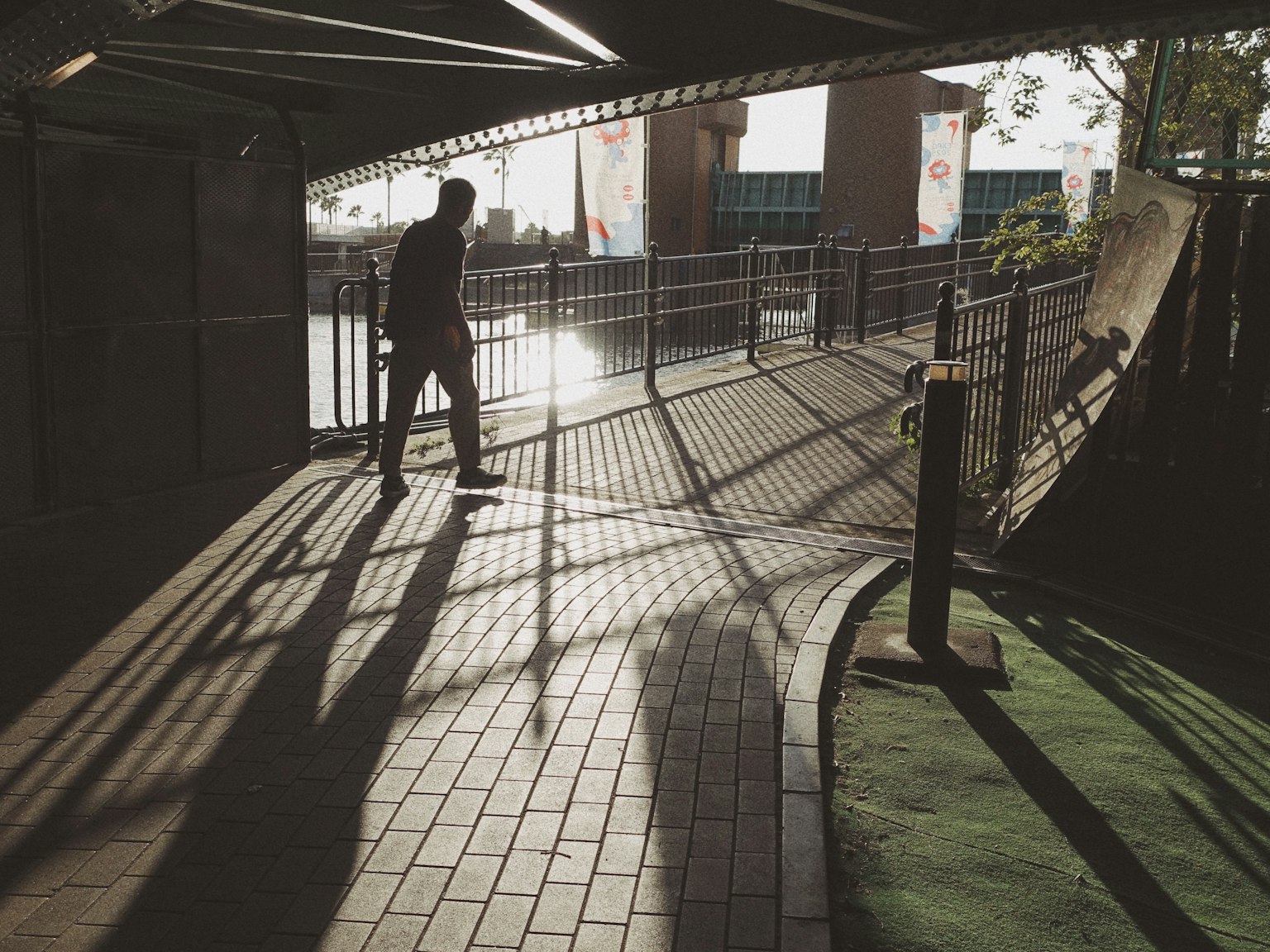 Silhouette einer Person, die auf einem schattigen Weg mit umliegenden Strukturen geht