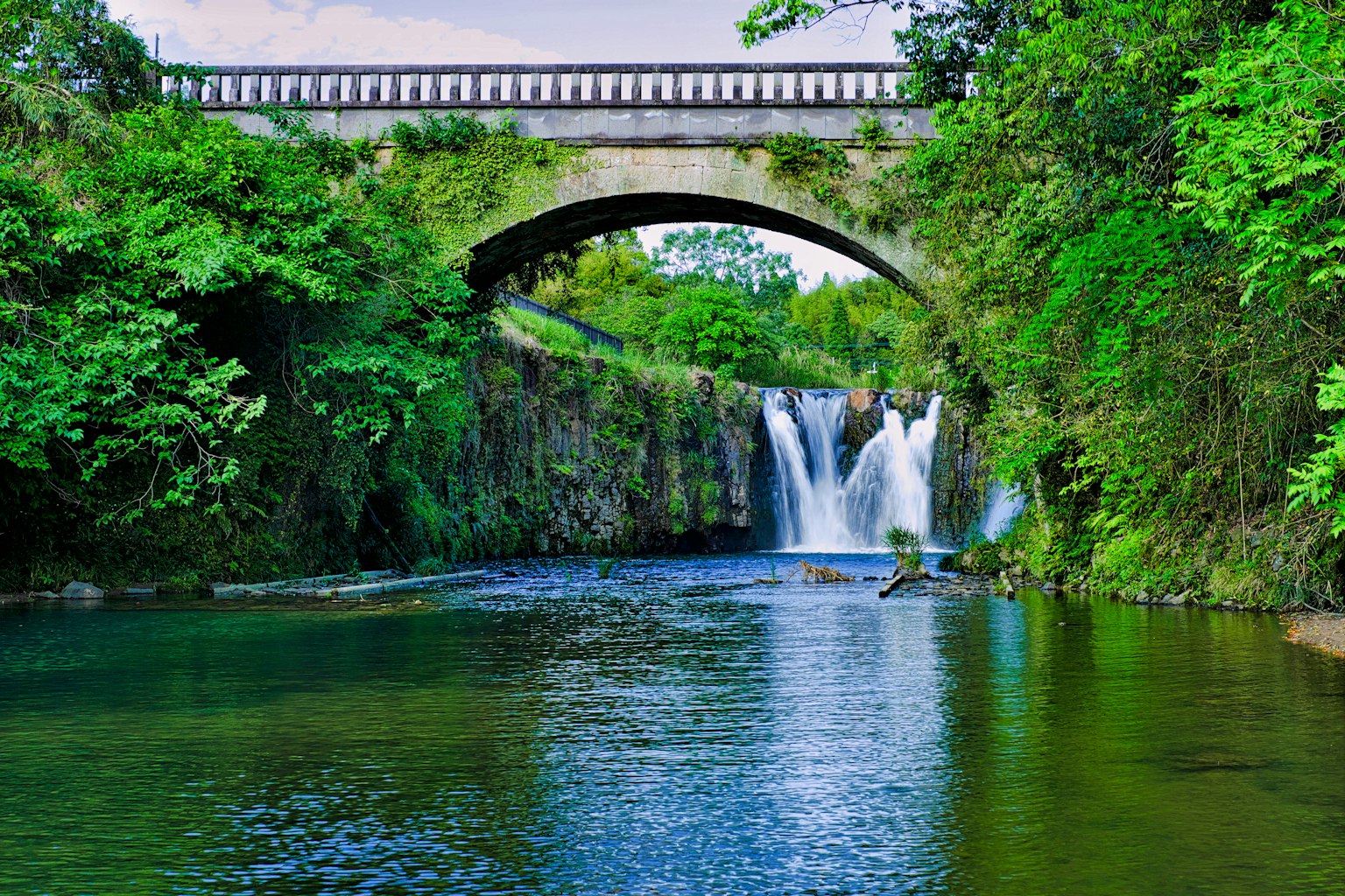 Vue pittoresque d'une cascade sous un pont entouré de verdure luxuriante