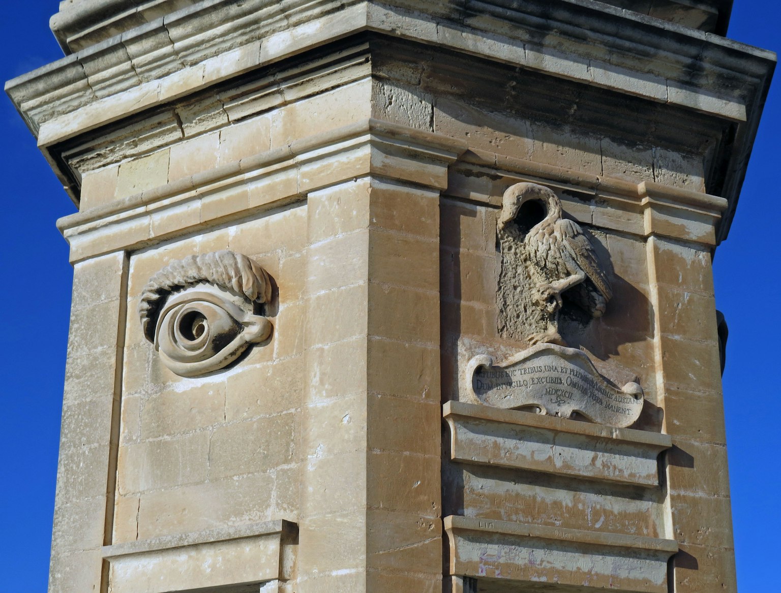 Sculpturale Details eines Auges und einer Nase auf einer Steinsäule vor blauem Himmel