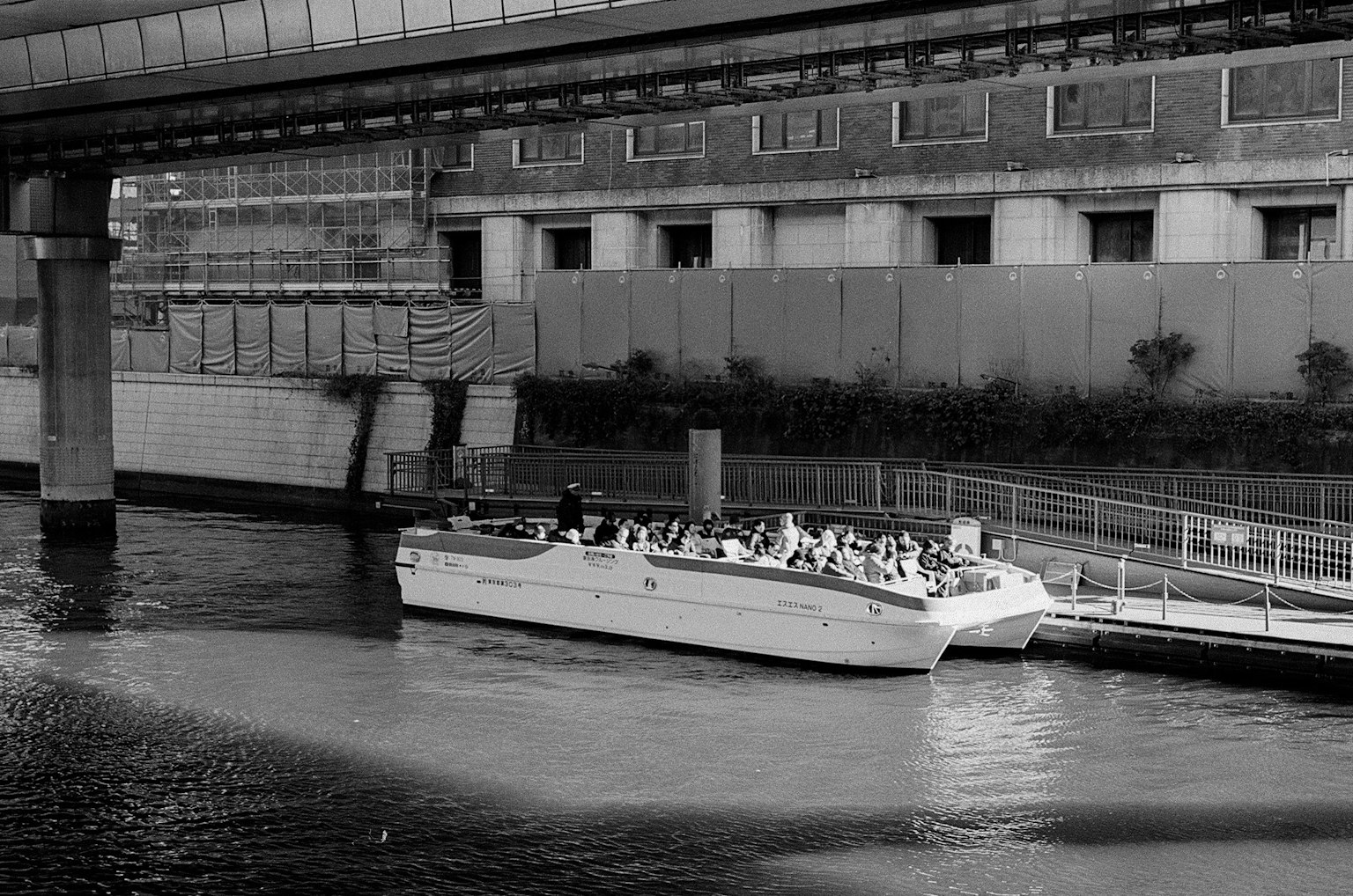 Image en noir et blanc d'un bateau amarré sur une rivière avec des bâtiments environnants