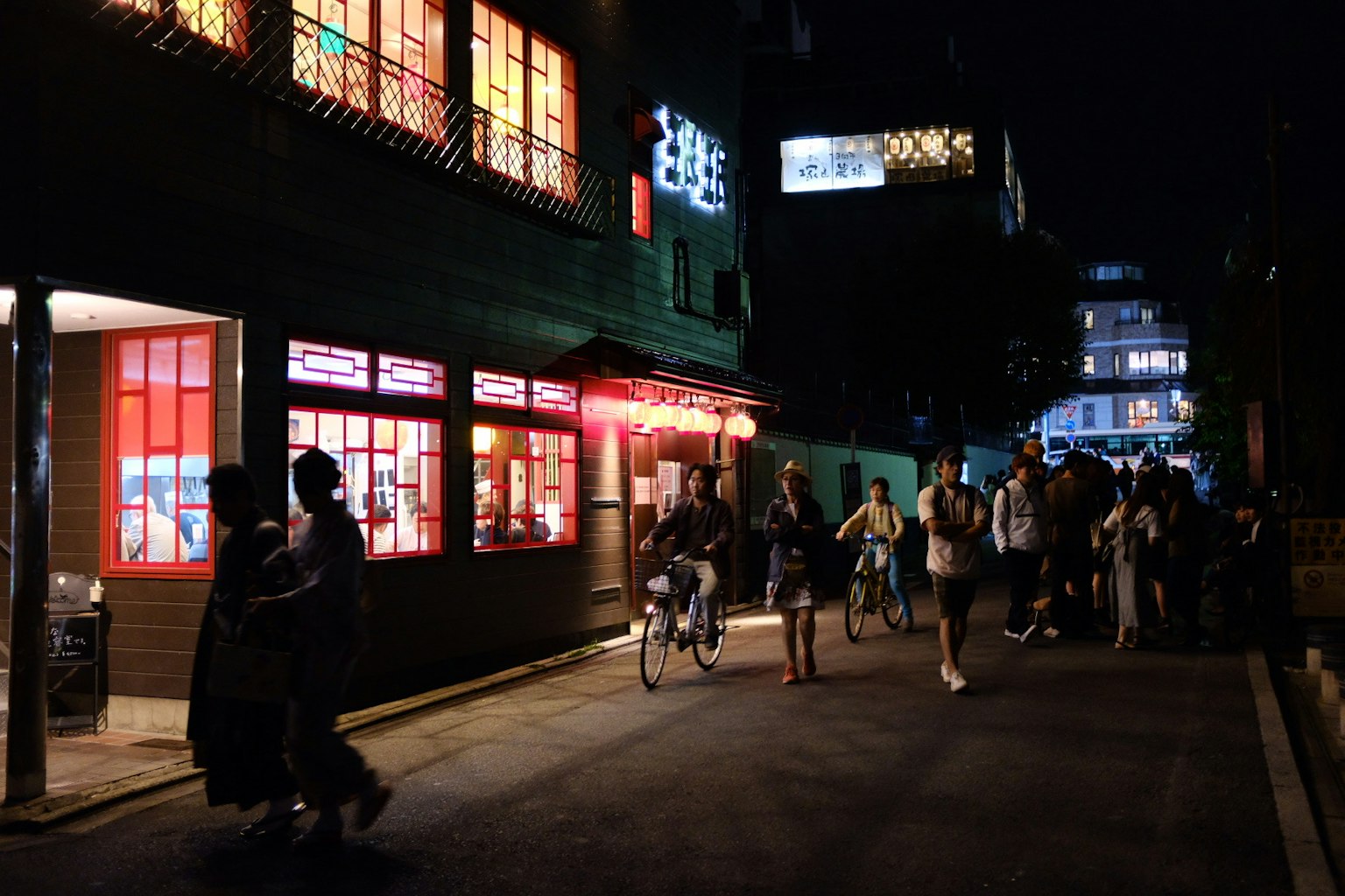 Scène de rue animée la nuit avec un restaurant aux fenêtres rouges et des piétons