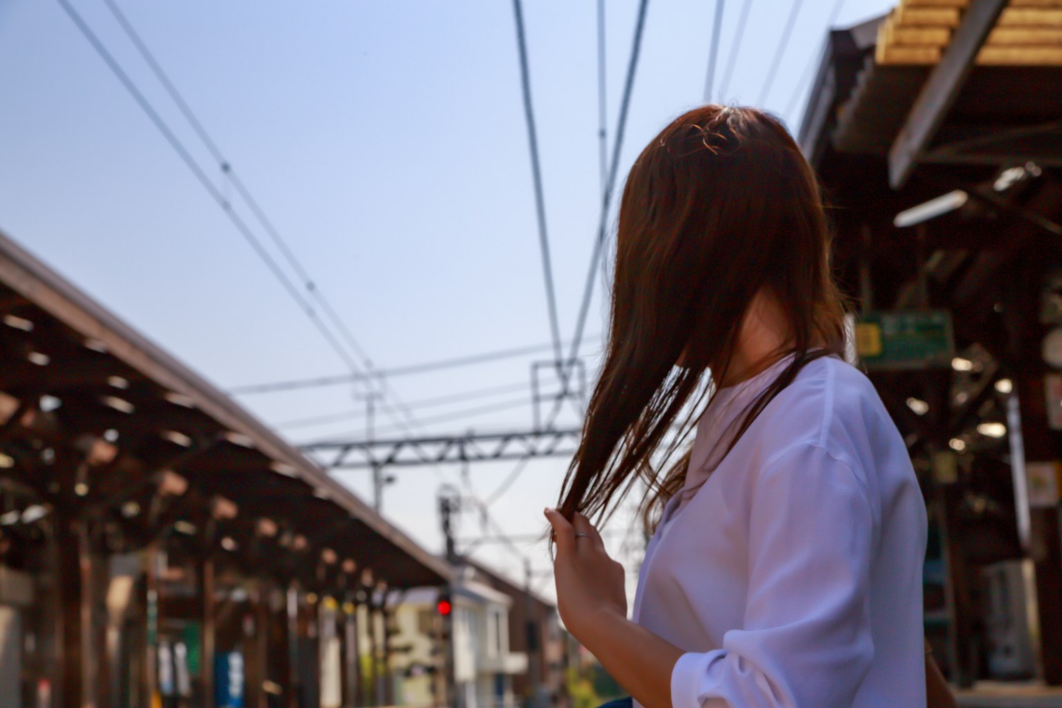 A woman stands on a train platform touching her hair