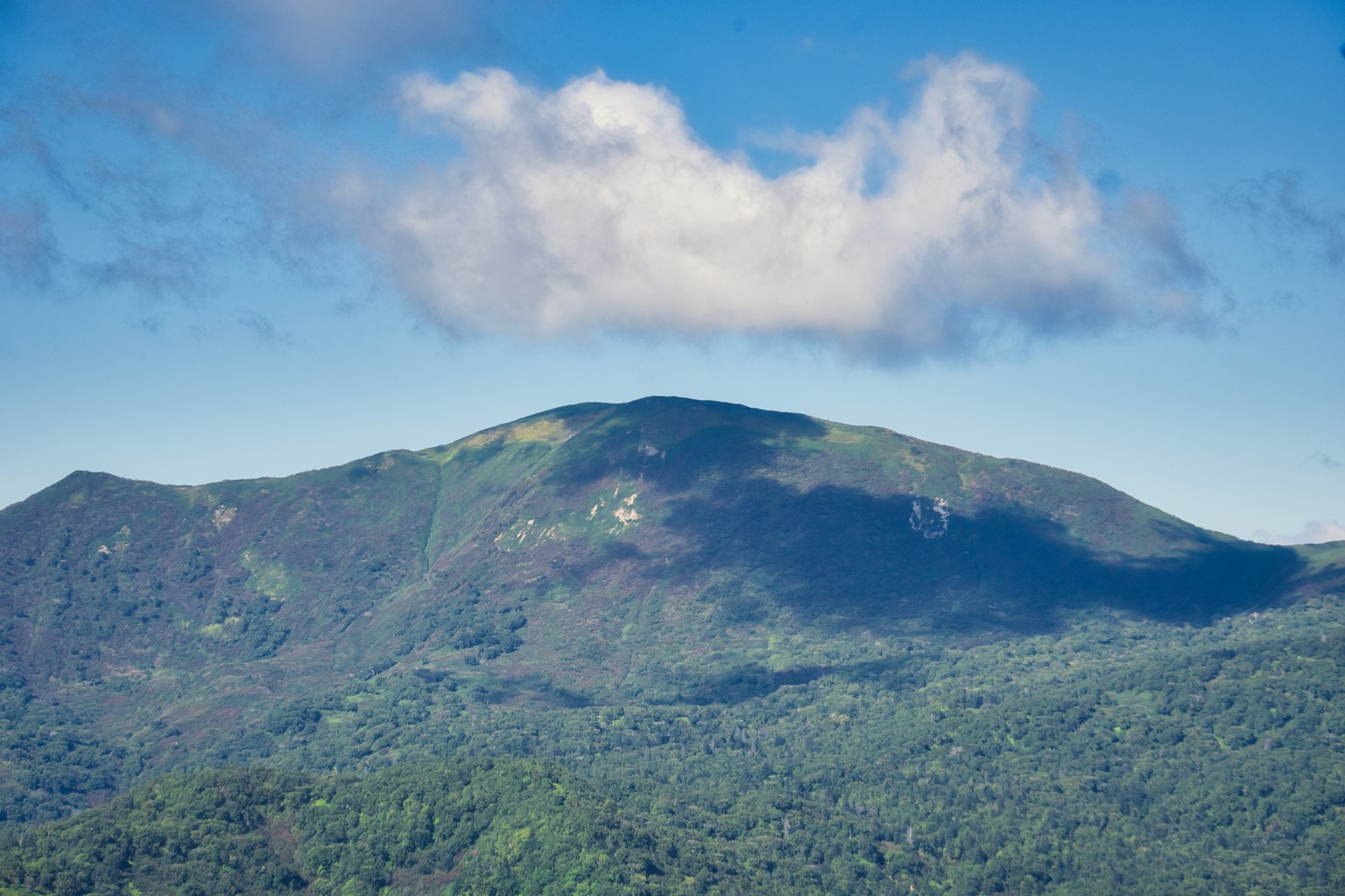 Paisaje montañoso verde bajo un cielo azul con nubes blancas