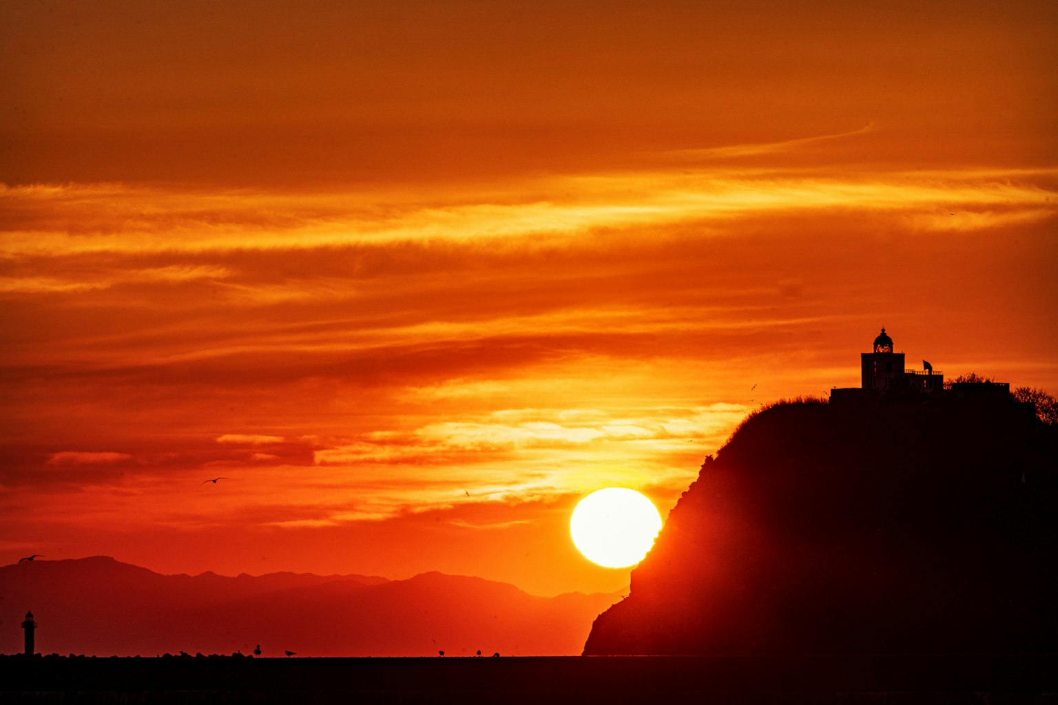 Sonnenuntergang über einem Berg mit einem Leuchtturm