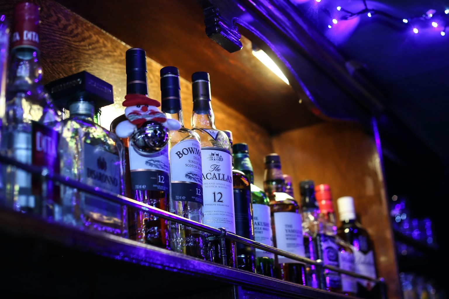 A shelf of assorted liquor bottles illuminated by blue-purple lights