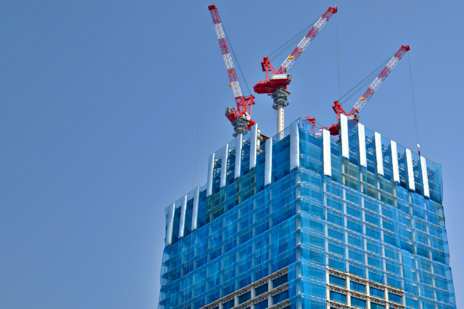 Cantiere di costruzione di un grattacielo coperto da un telo blu con gru in cima