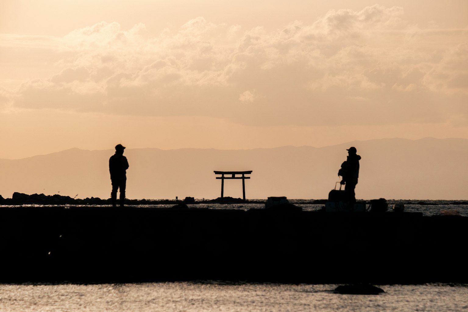 Siluetas de dos personas contra un atardecer con un torii