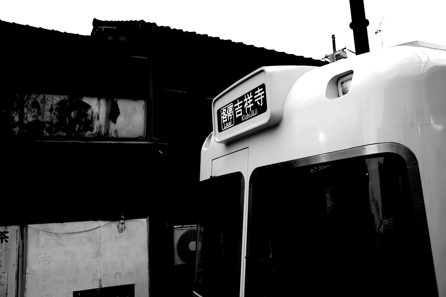 Black and white image of a bus with a Japanese sign and an old building in the background
