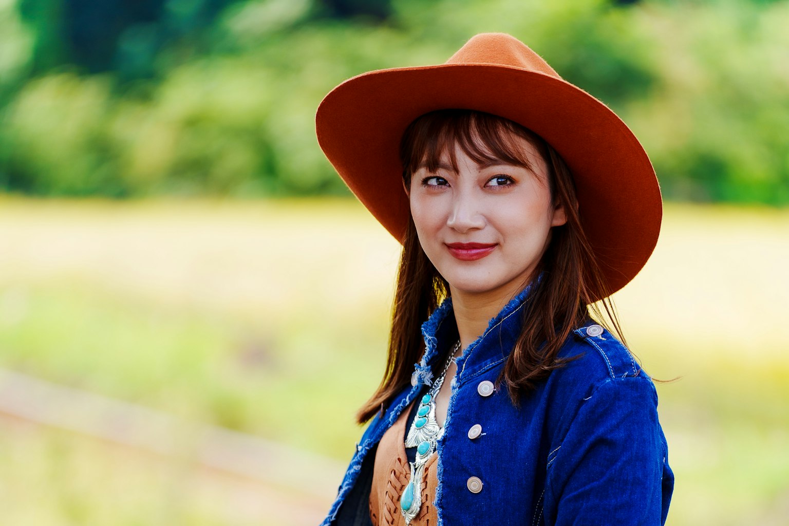 Woman wearing a denim jacket and orange hat smiling in a scenic background