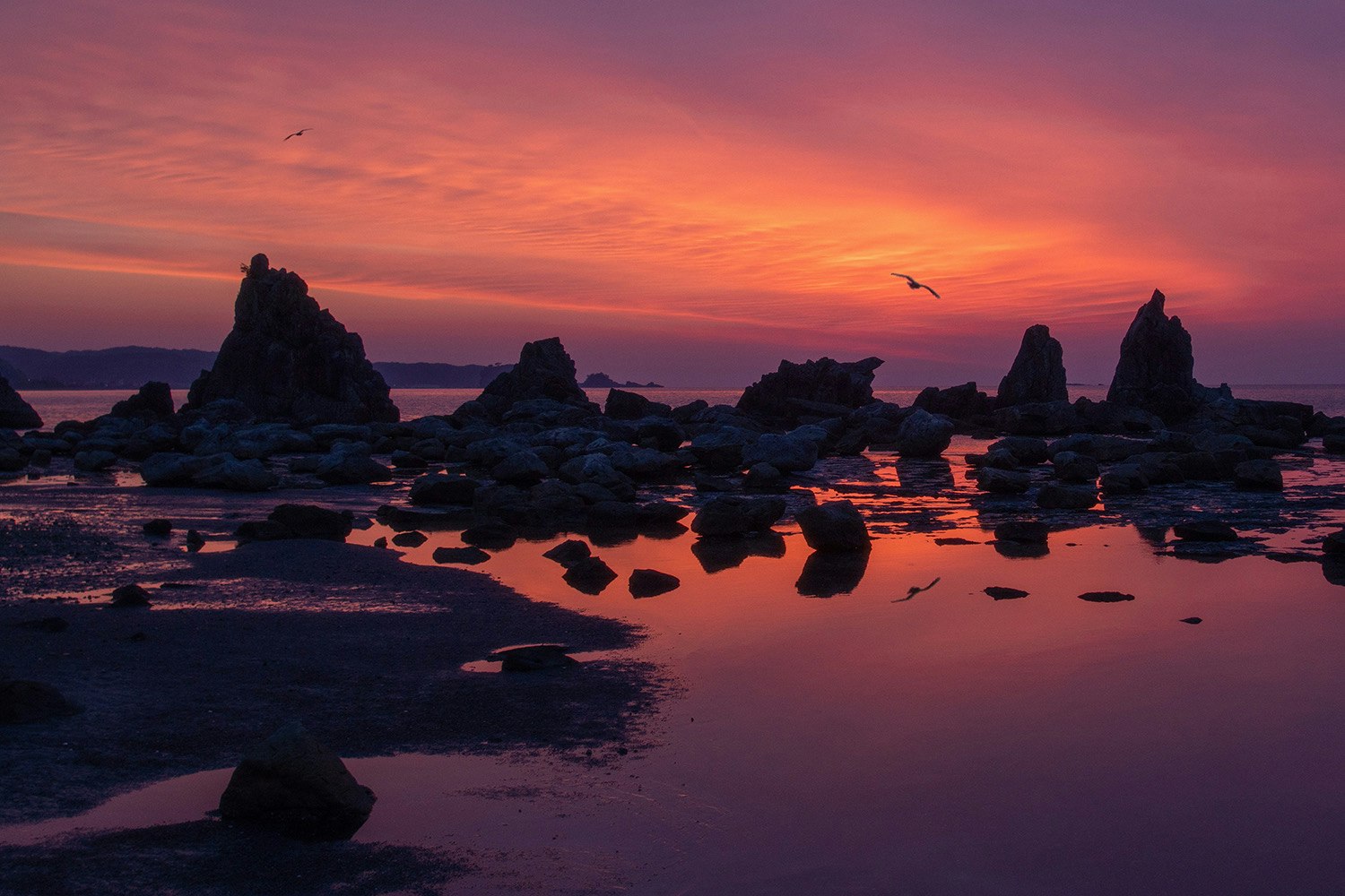 felsige Küste bei Sonnenuntergang mit Felsen und Spiegelungen