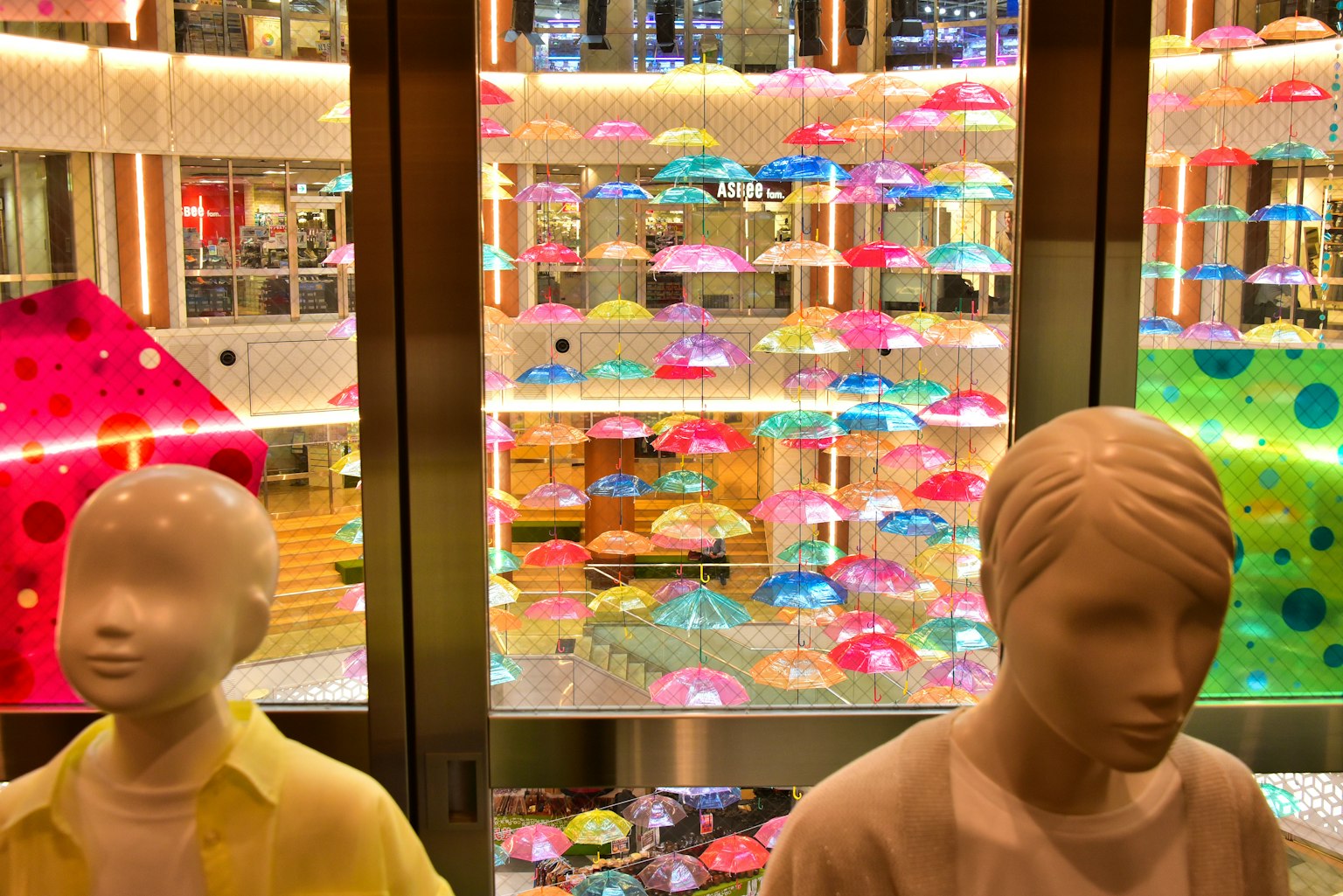 Parapluies colorés exposés dans une vitrine avec des mannequins