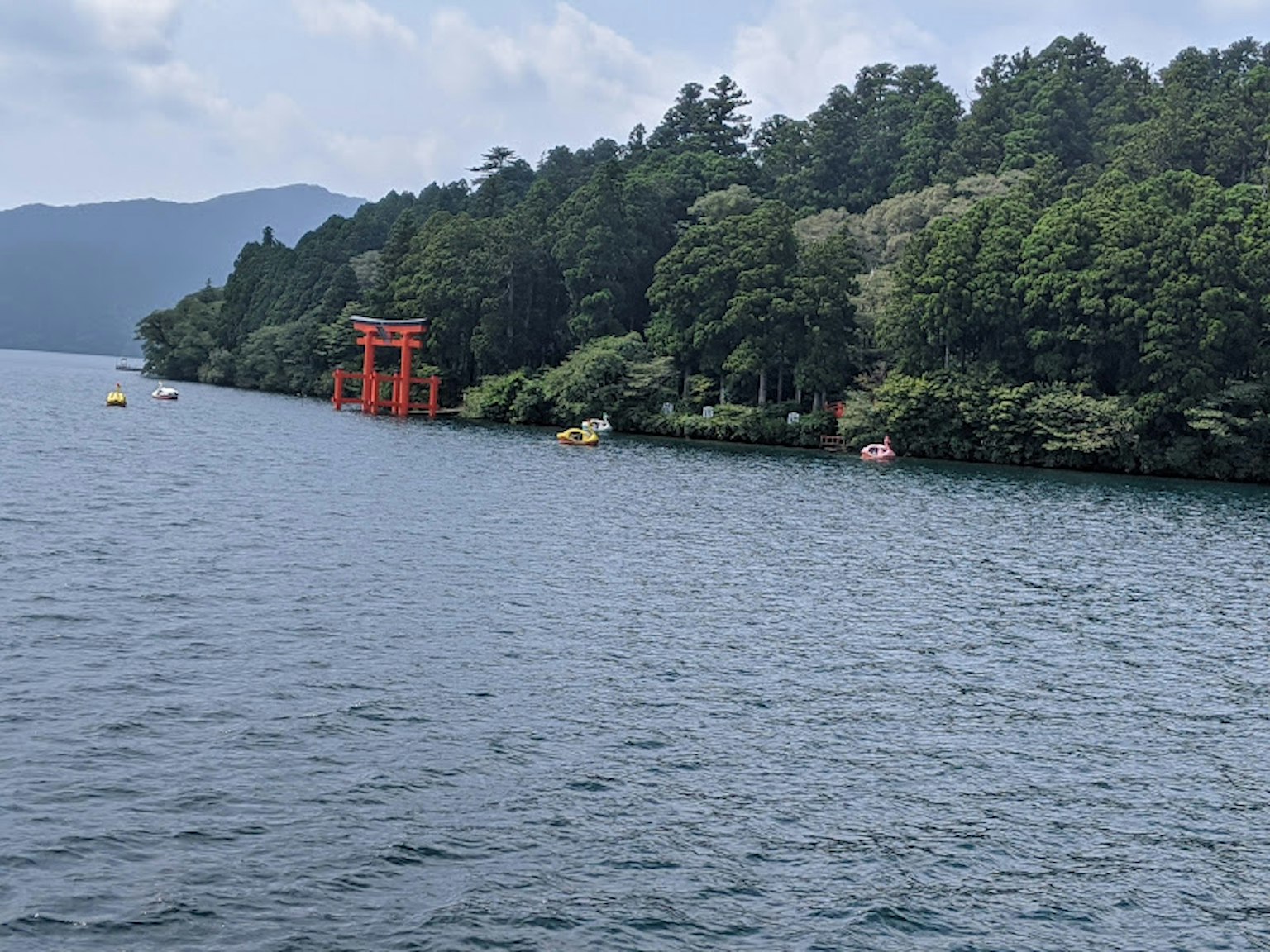 Rotes Torii am Ufer eines ruhigen Sees umgeben von üppigem Grün