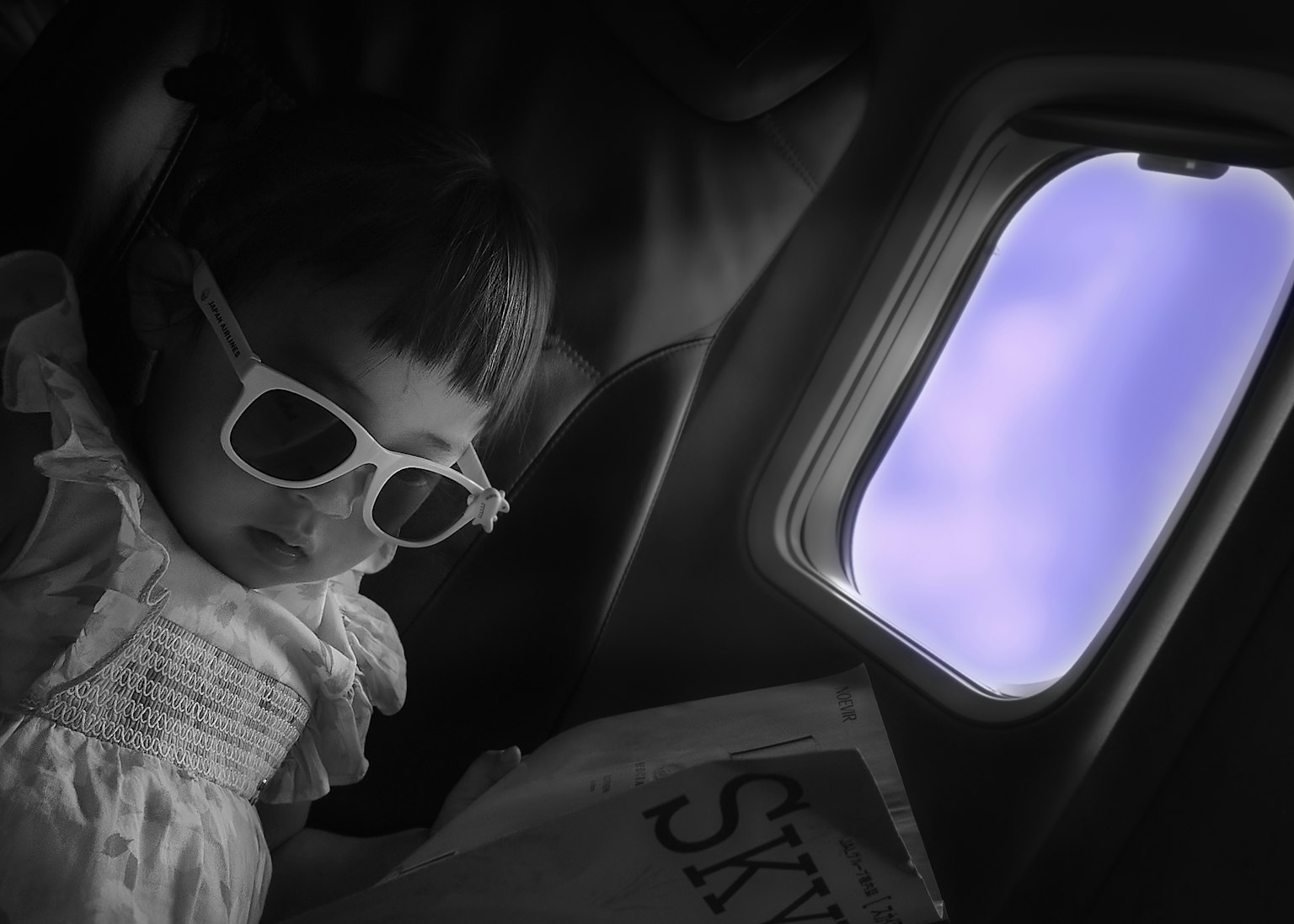 Bambino con occhiali da sole che legge un libro su un aereo