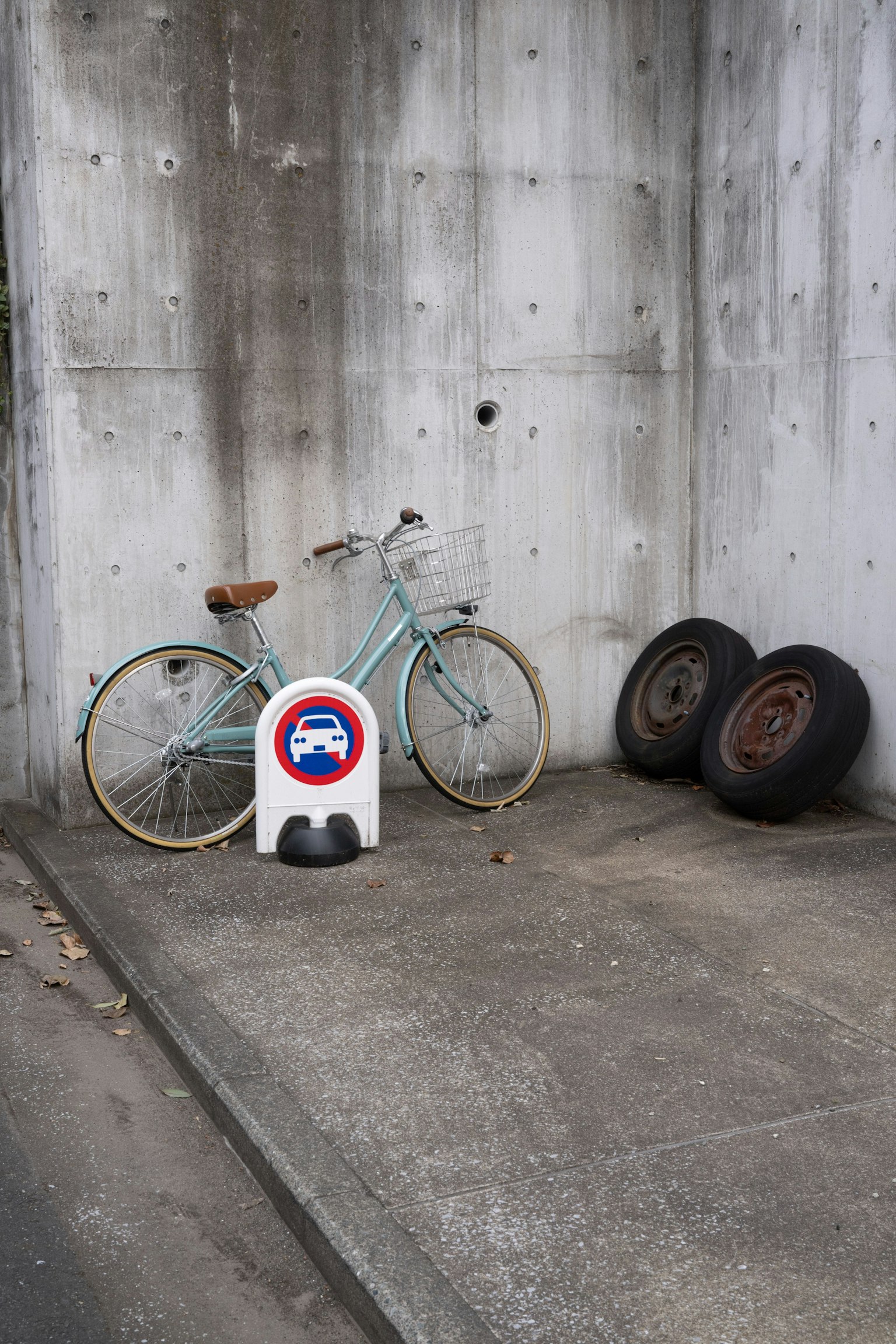 Un vélo bleu adossé à un mur en béton à côté d'un ensemble de vieux pneus