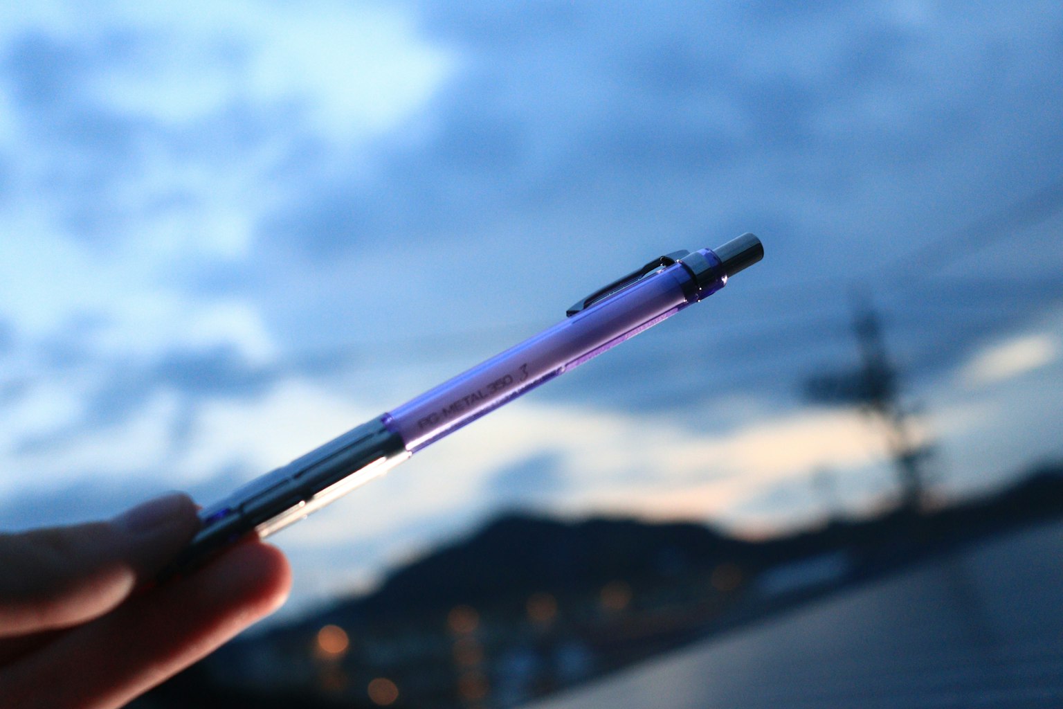 Hand hält einen lila Tintenstift vor einem Dämmerungshimmel