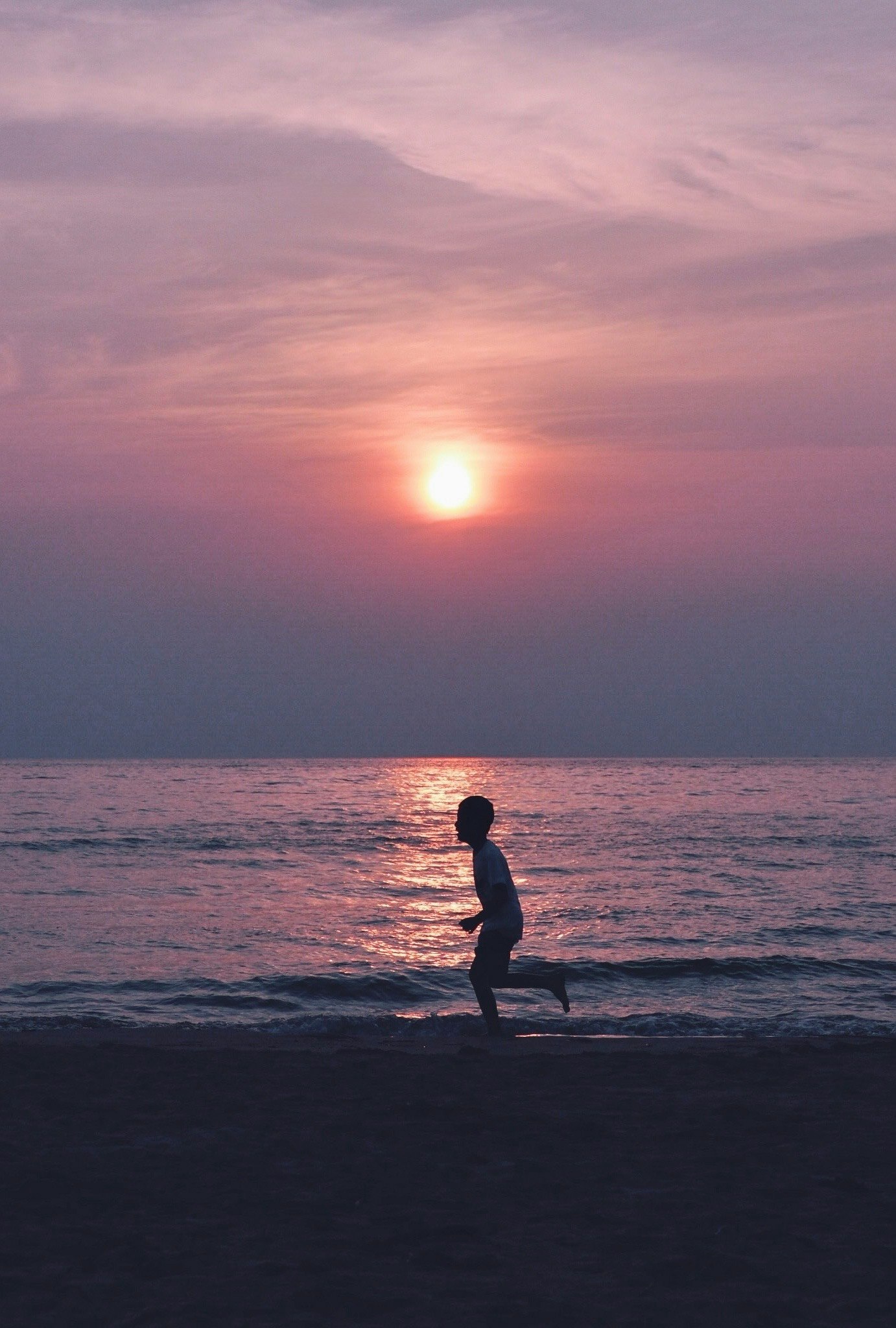 夕暮れの海辺で歩くシルエットの人物