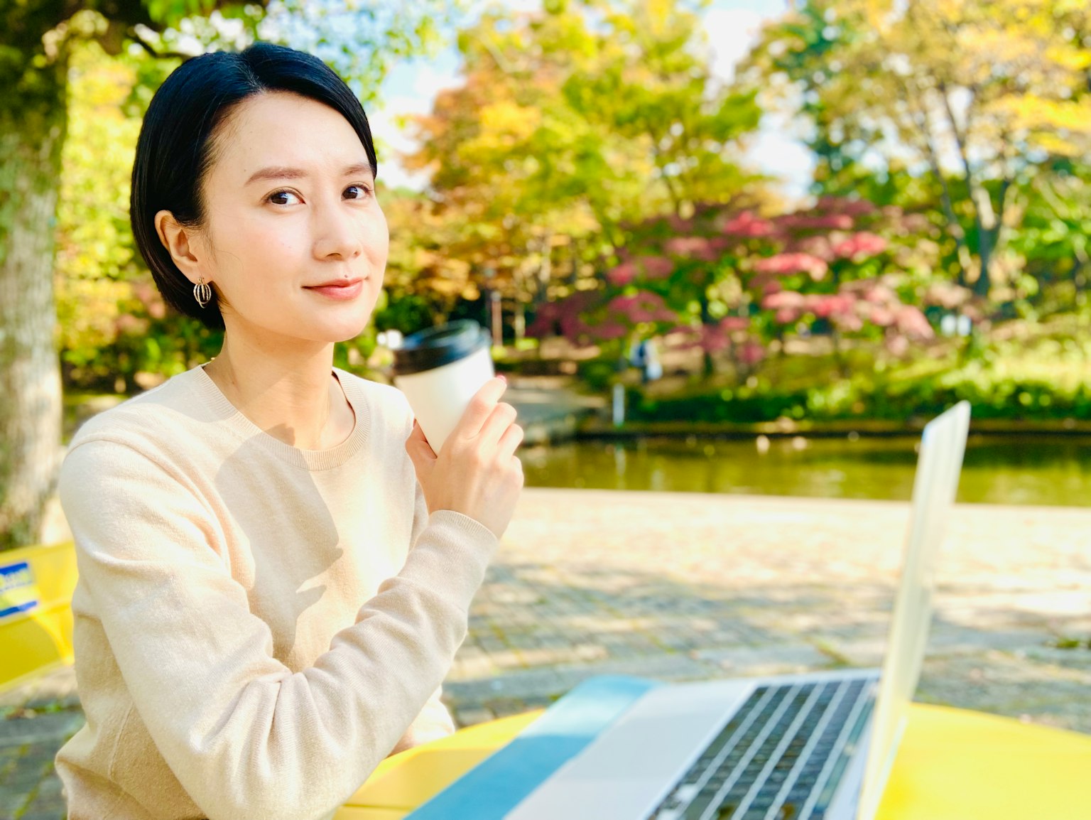 女性在公园里拿着咖啡使用笔记本电脑