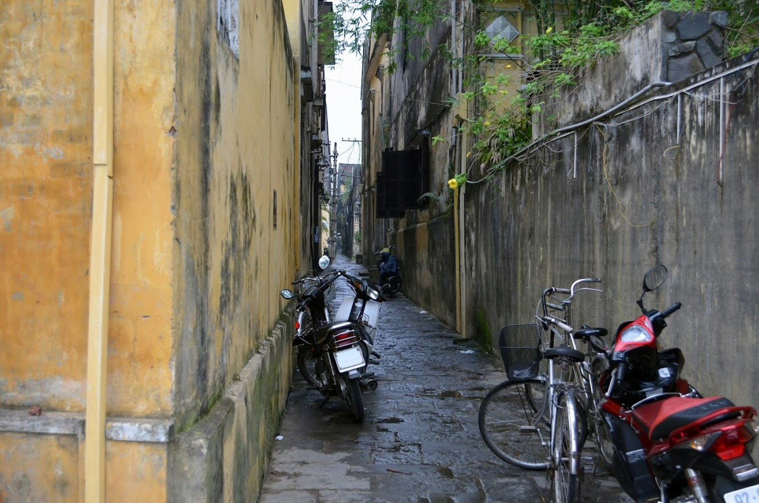Callejón estrecho con motocicletas y bicicletas estacionadas rodeado de viejas paredes de edificio