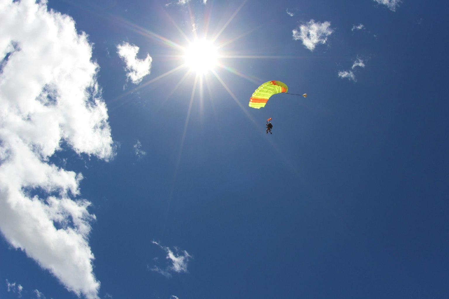 Paraglider terbang di langit biru dengan sinar matahari yang cerah