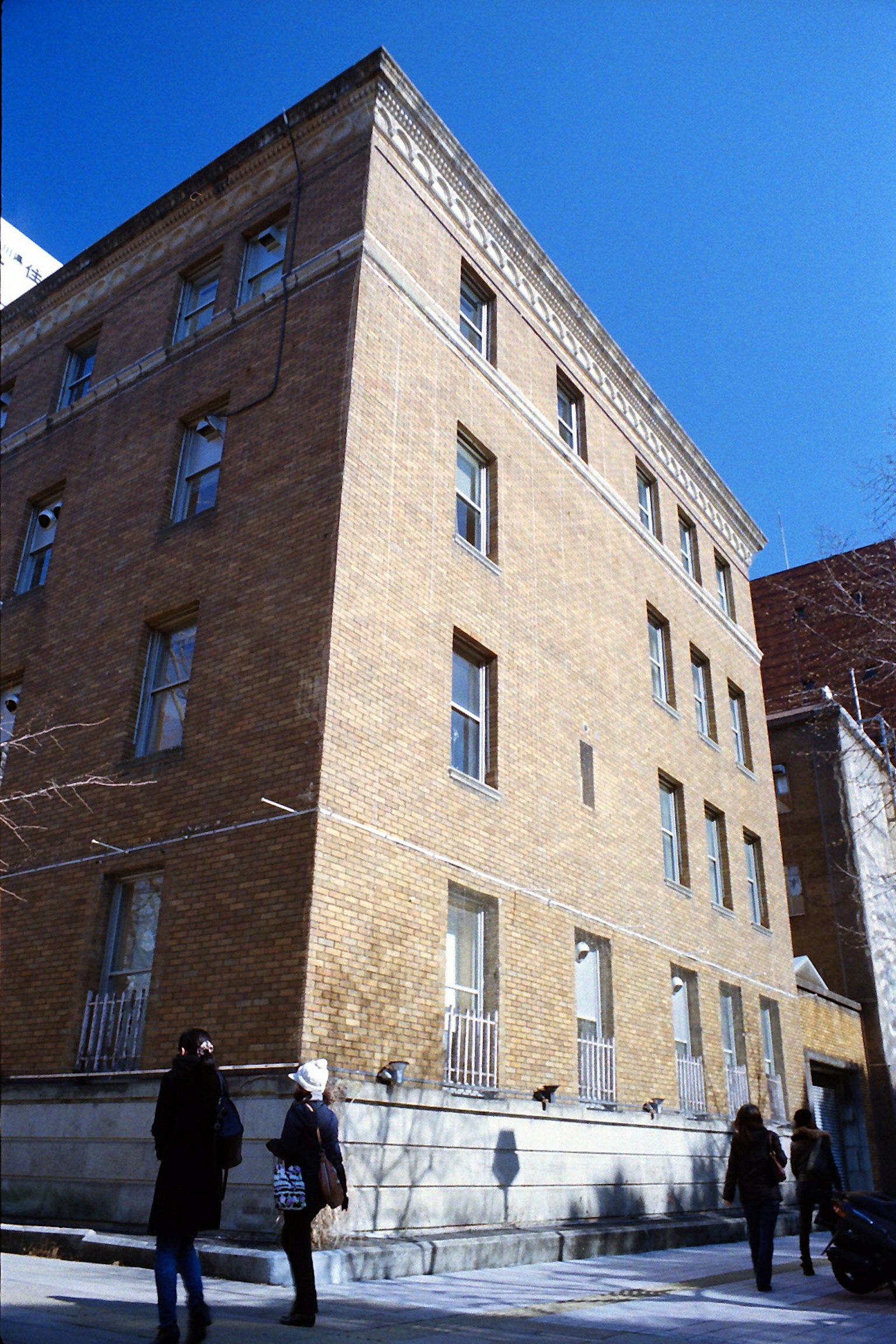 Brick building under a blue sky with pedestrians