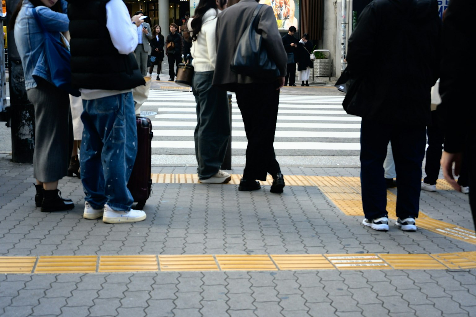 横断歩道で待つ人々の足元の写真 交差点の様子が見える