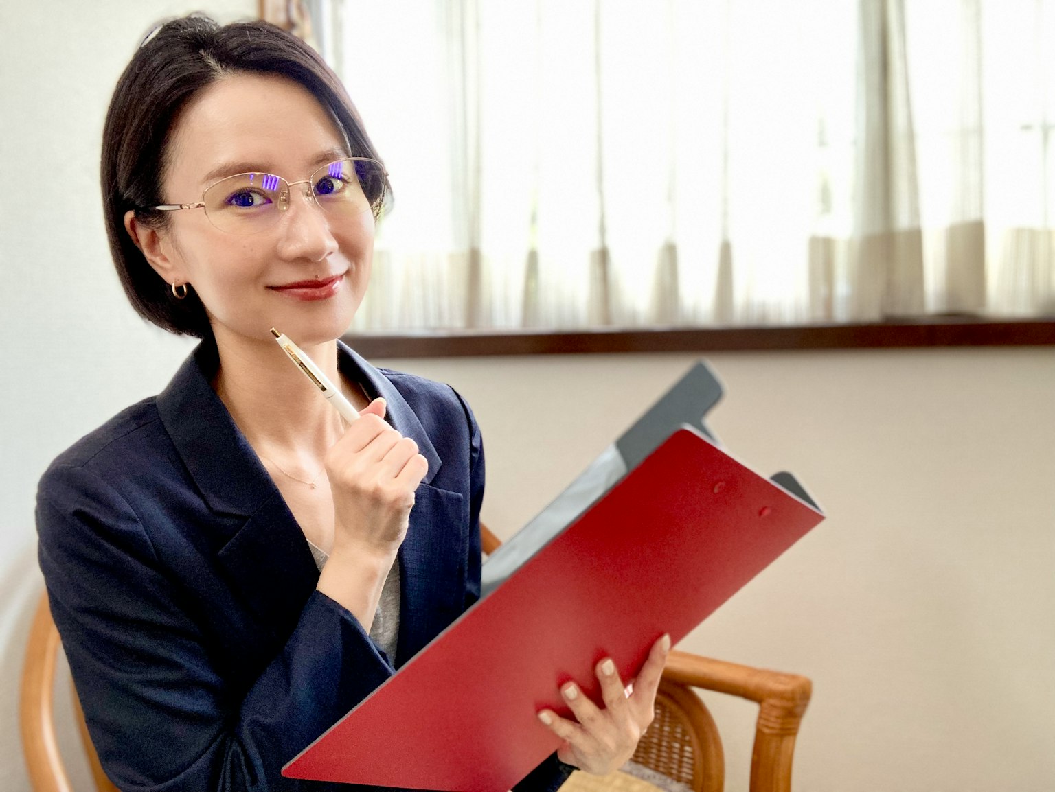 Wanita memegang folder merah dan pena tersenyum di lingkungan kantor