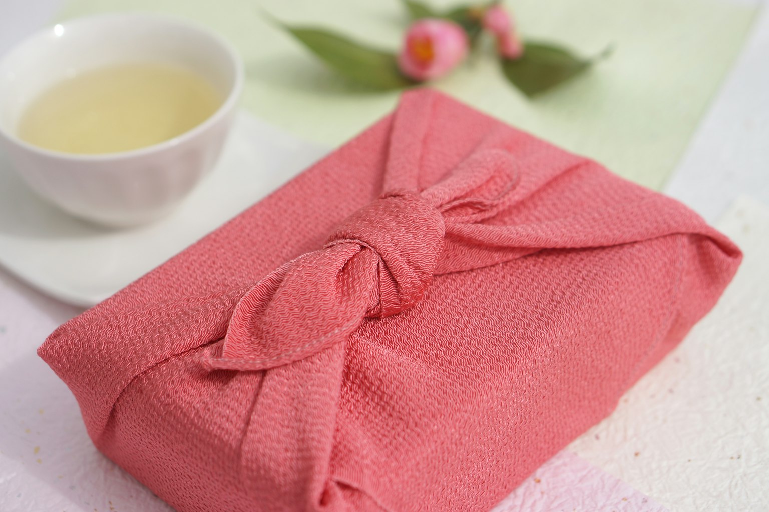 Un regalo avvolto in un tessuto rosa accanto a una ciotola di tè bianca