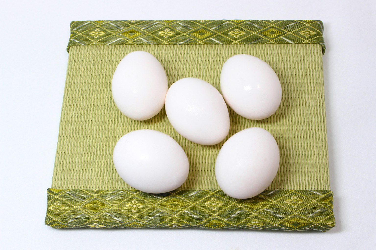 Five white eggs arranged on a green patterned mat
