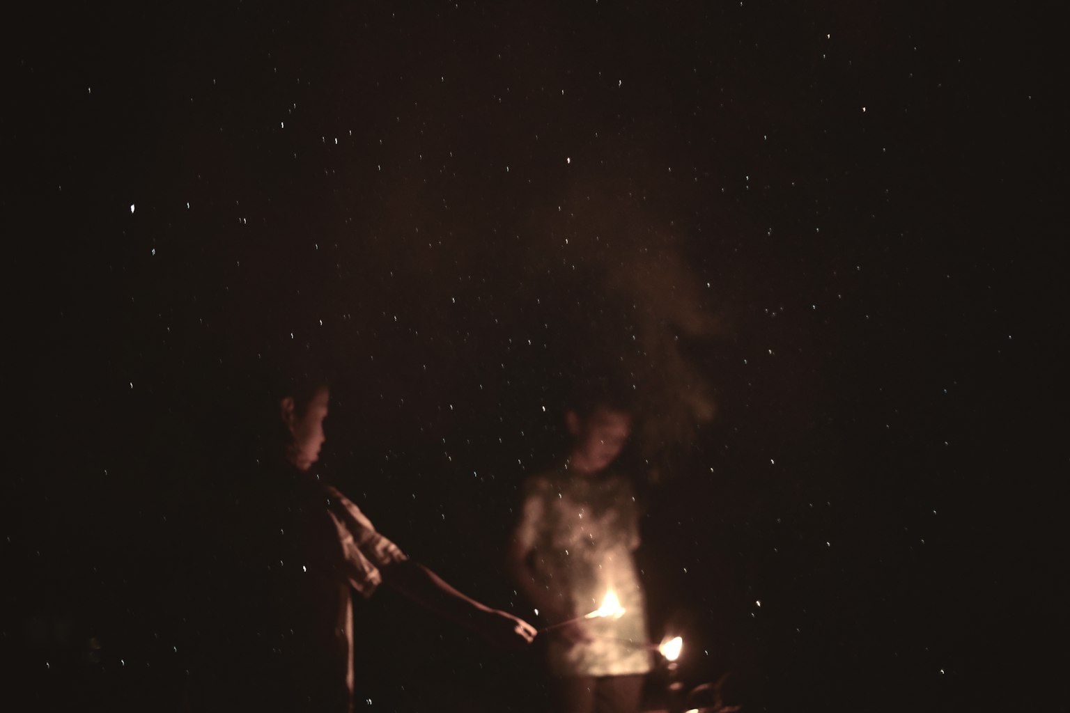 Two people gathered around a fire in a dark setting with smoke