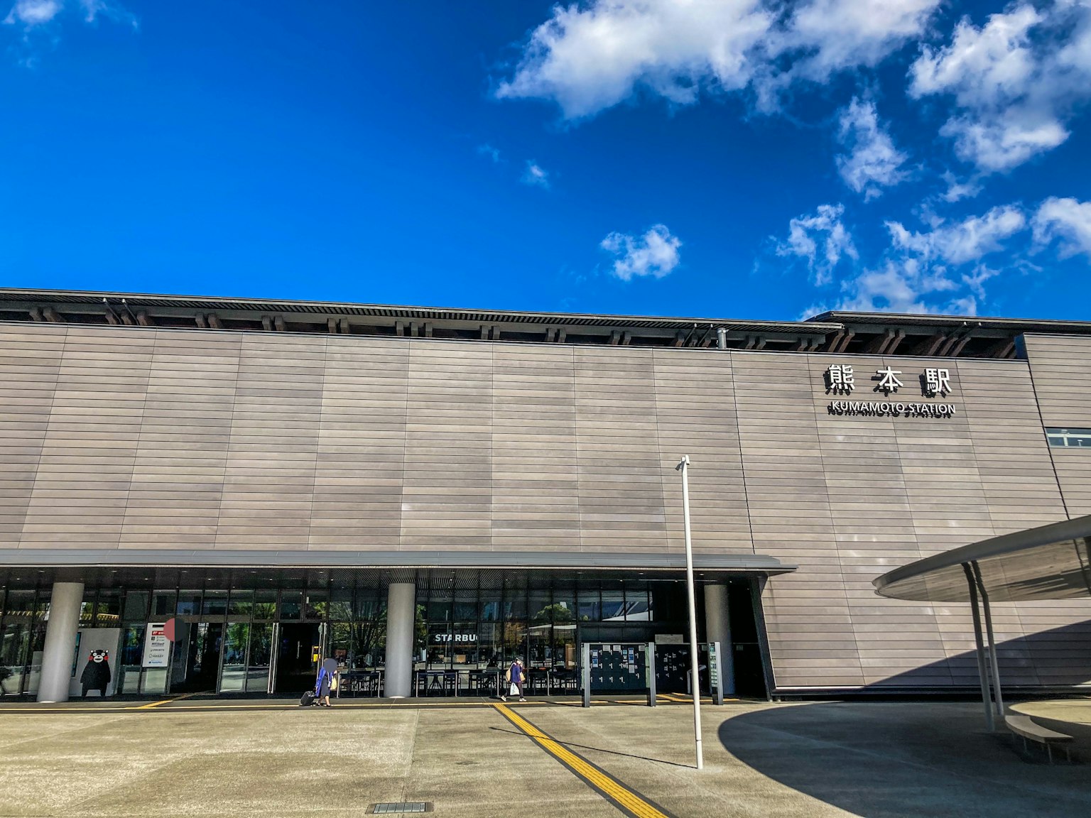 Modern train station exterior under blue sky featuring gray walls and large glass windows