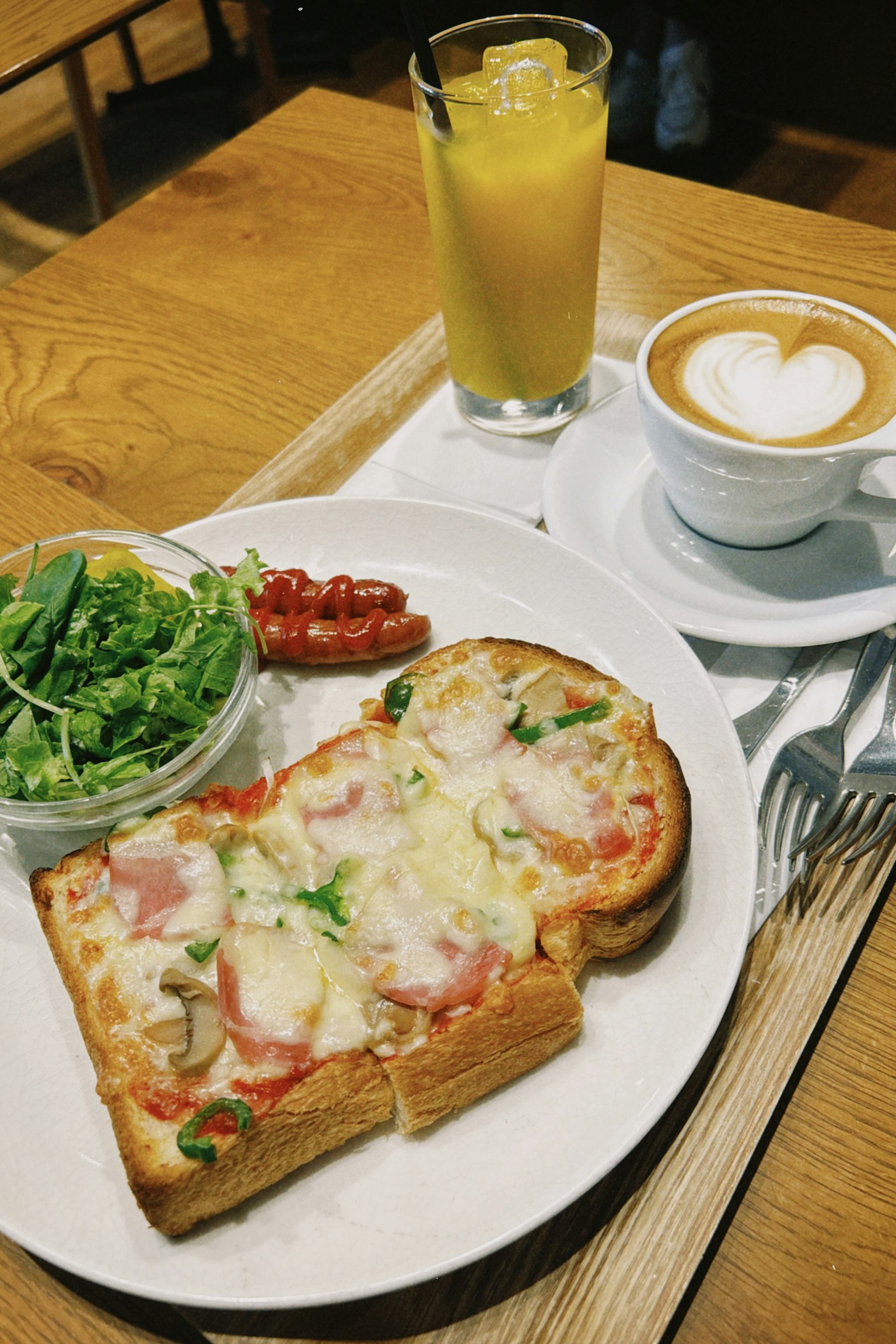 Toast con formaggio e prosciutto servito con insalata e salsiccia accanto a un latte macchiato a forma di cuore