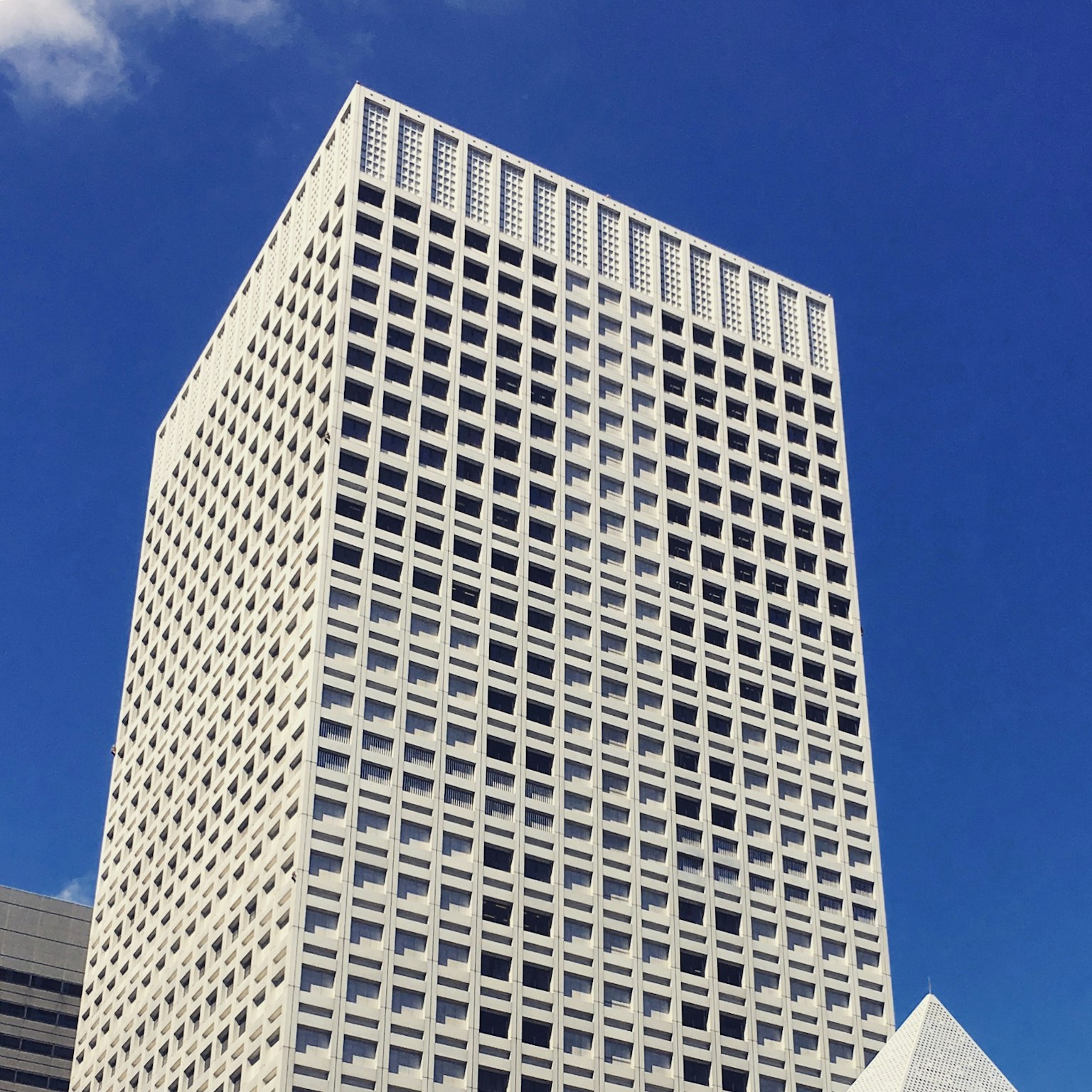 Hoher weißer Wolkenkratzer mit Gitterfassade vor blauem Himmel