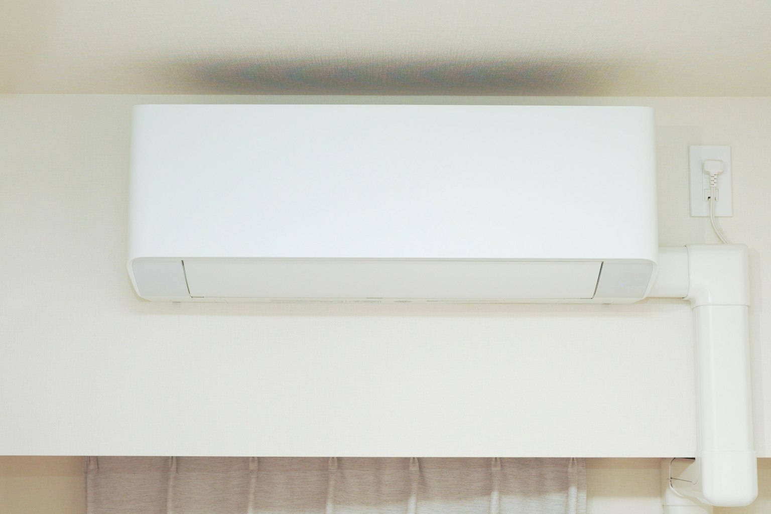 A white air conditioner mounted on a wall in a simple indoor setting