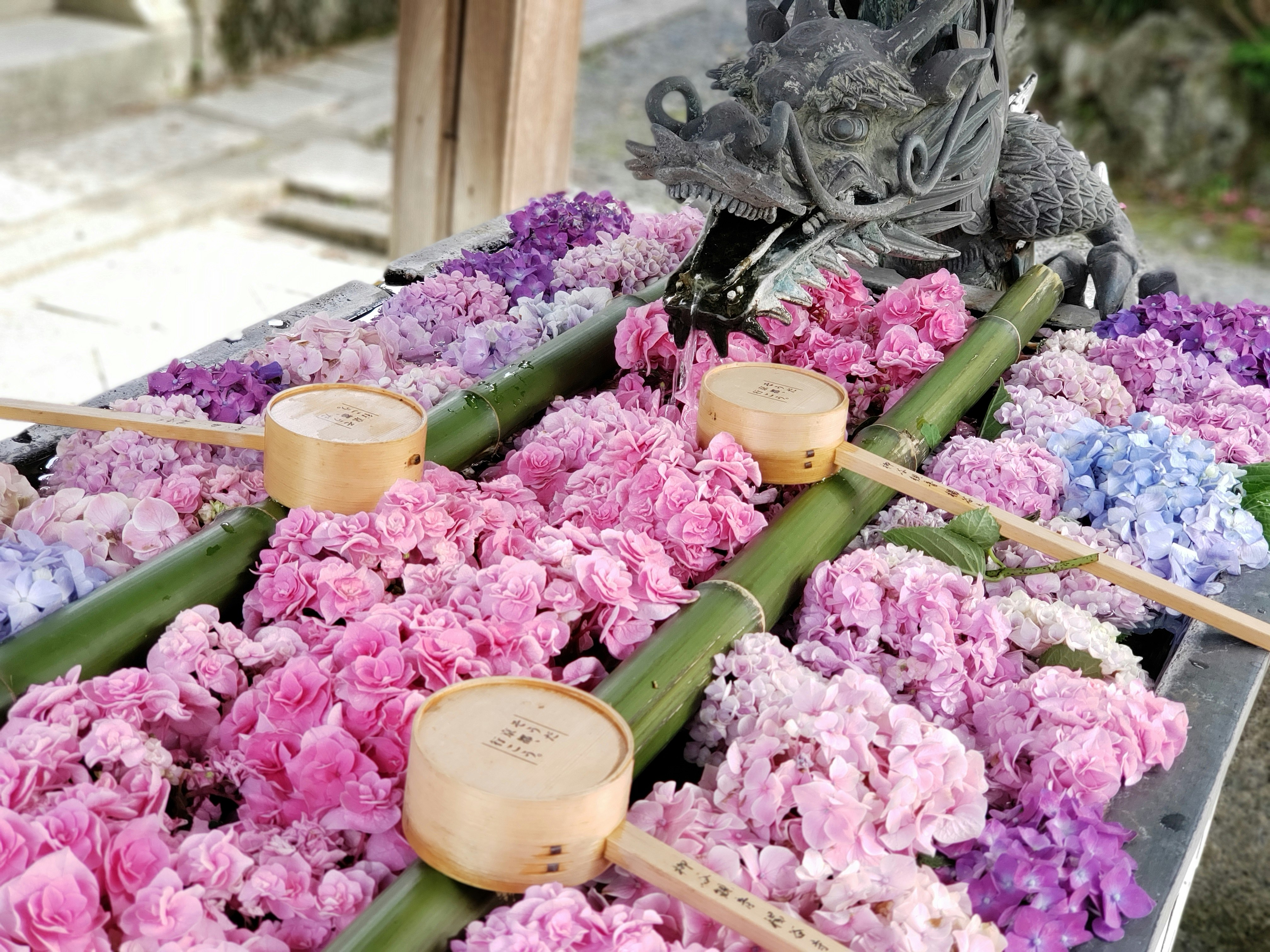 A dragon sculpture above a water basin decorated with pink flowers and bamboo