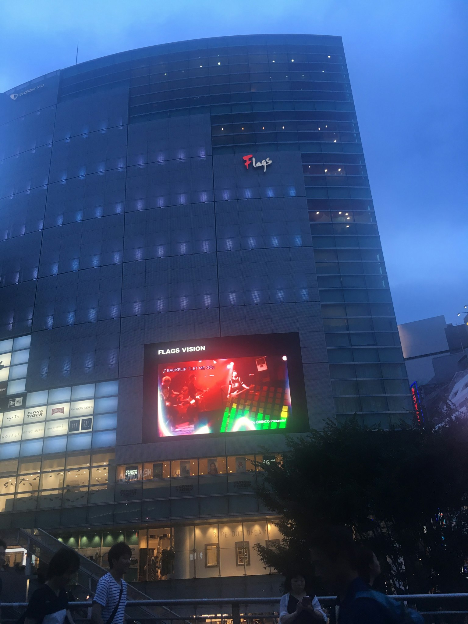 Building at dusk featuring large digital advertisement and surrounding people