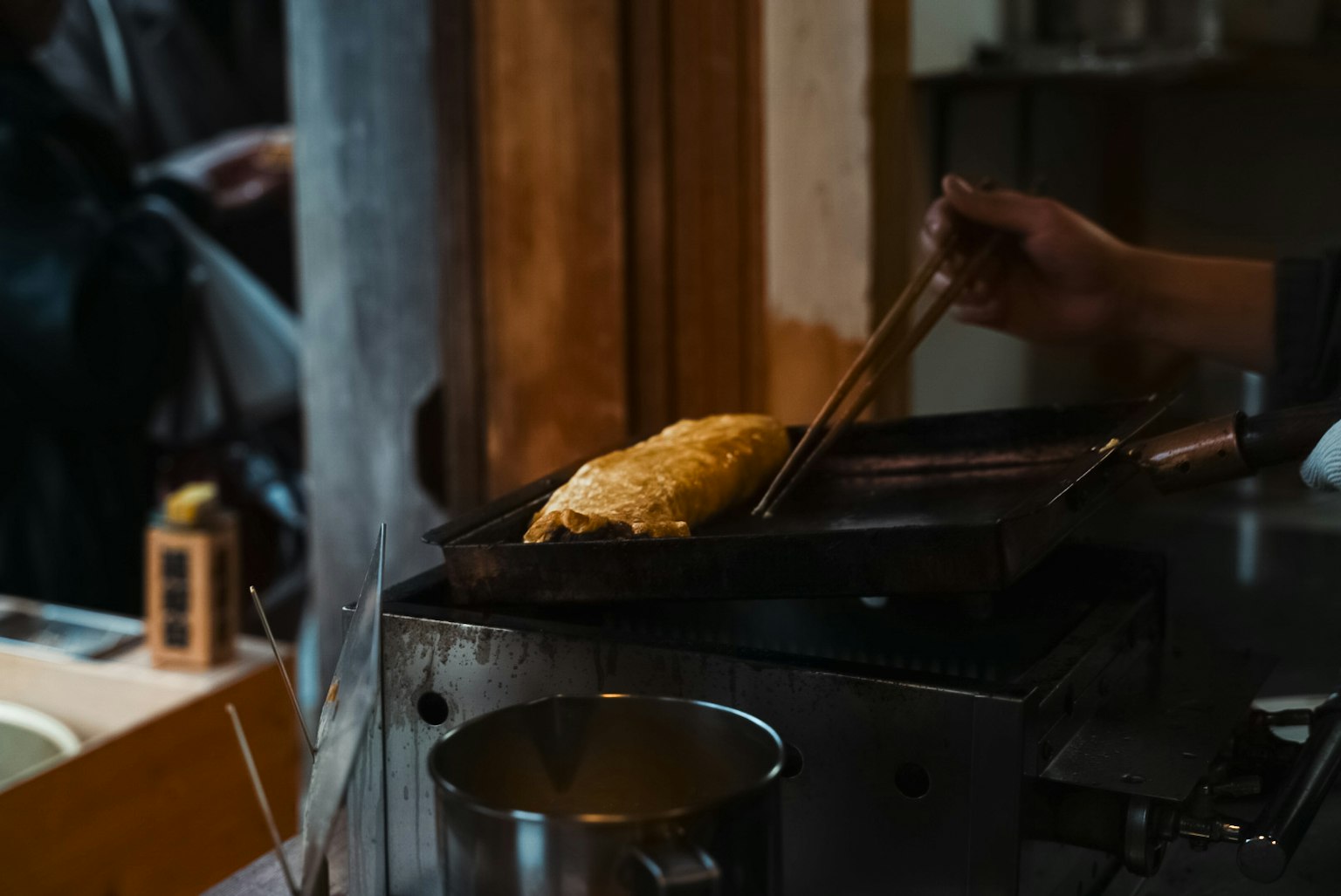 Close-up of a hand lifting a freshly cooked omelette with chopsticks