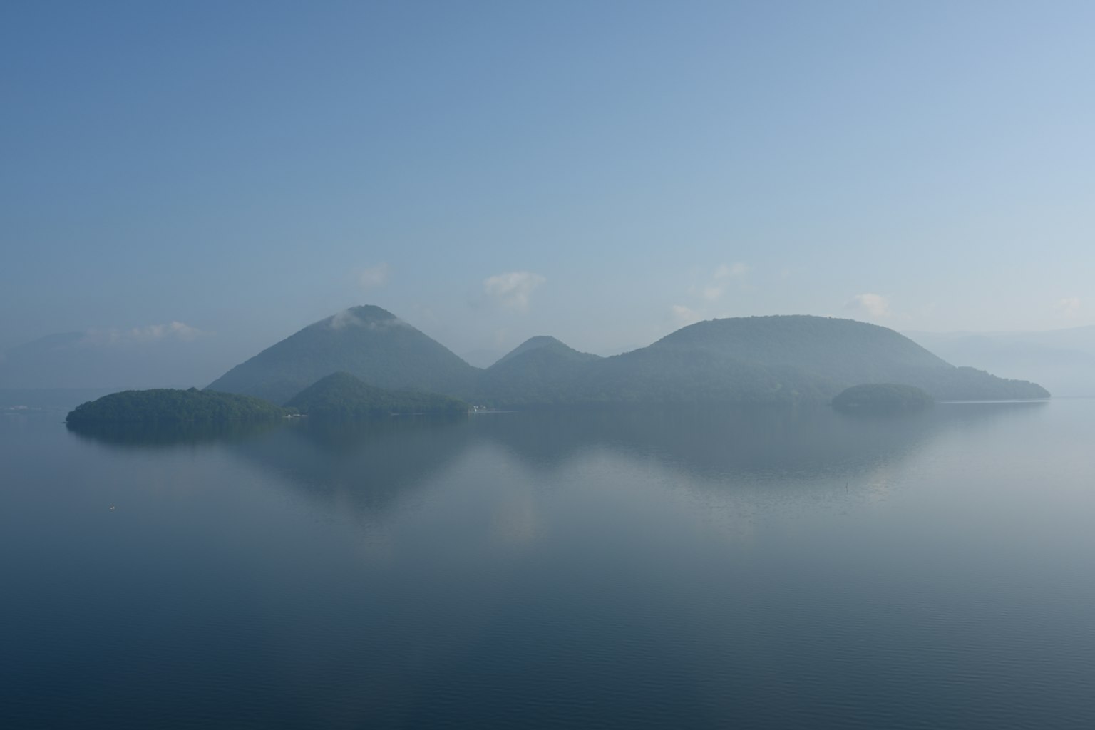 Landschaft von Inseln, die sich auf ruhigem Wasser in leichtem Nebel spiegeln