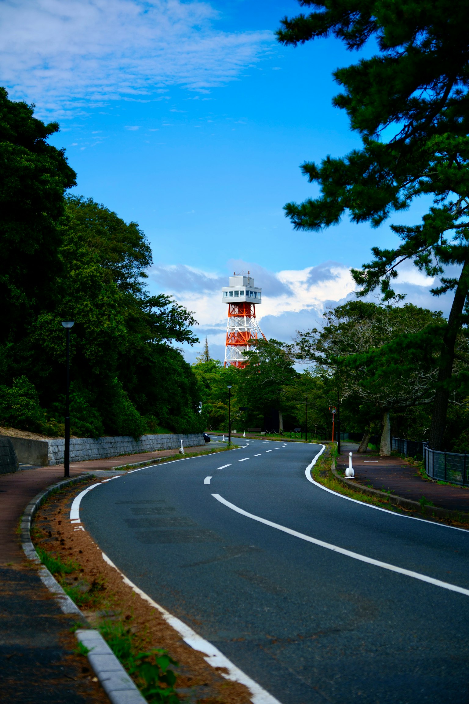 Route pittoresque serpentant à travers une végétation luxuriante avec un phare en arrière-plan