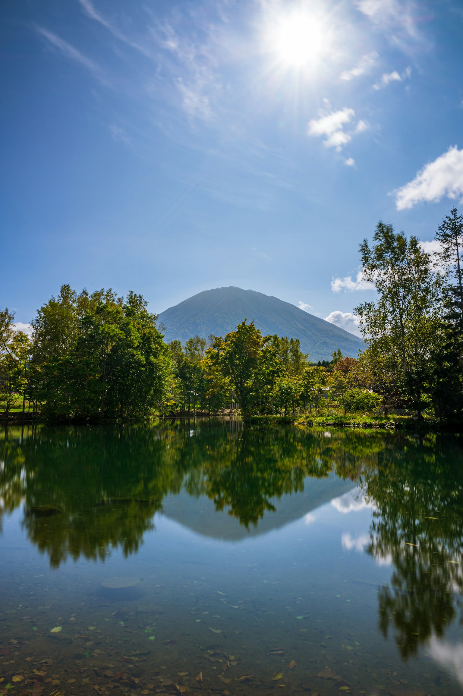 Danau tenang mencerminkan gunung dan langit biru