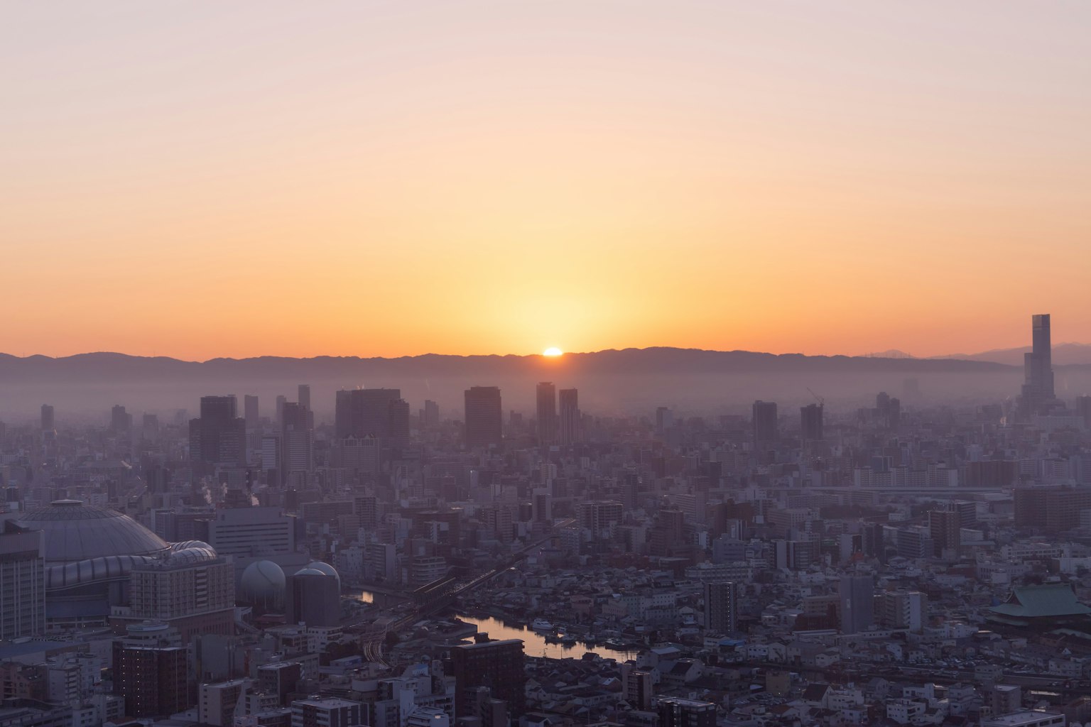 Panorama urbano all'alba con sole arancione brillante che sorge tra le montagne