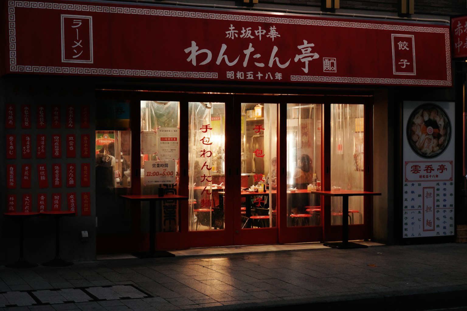 Exterior of a Chinese restaurant with red signage illuminated windows showing tables and chairs