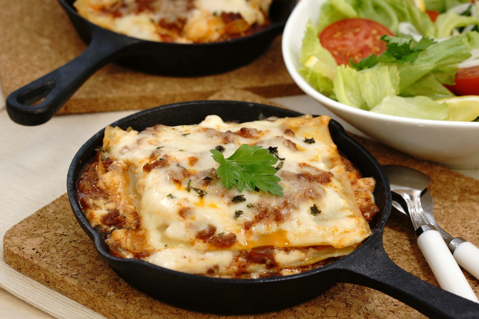 Lasagna servita in una padella con un'insalata fresca accanto