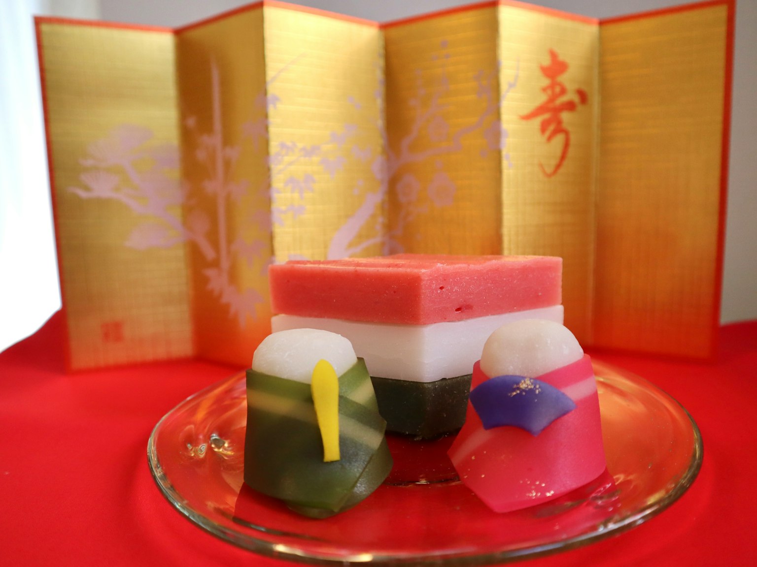 Dulces japoneses coloridos dispuestos en un plato de vidrio con un biombo dorado