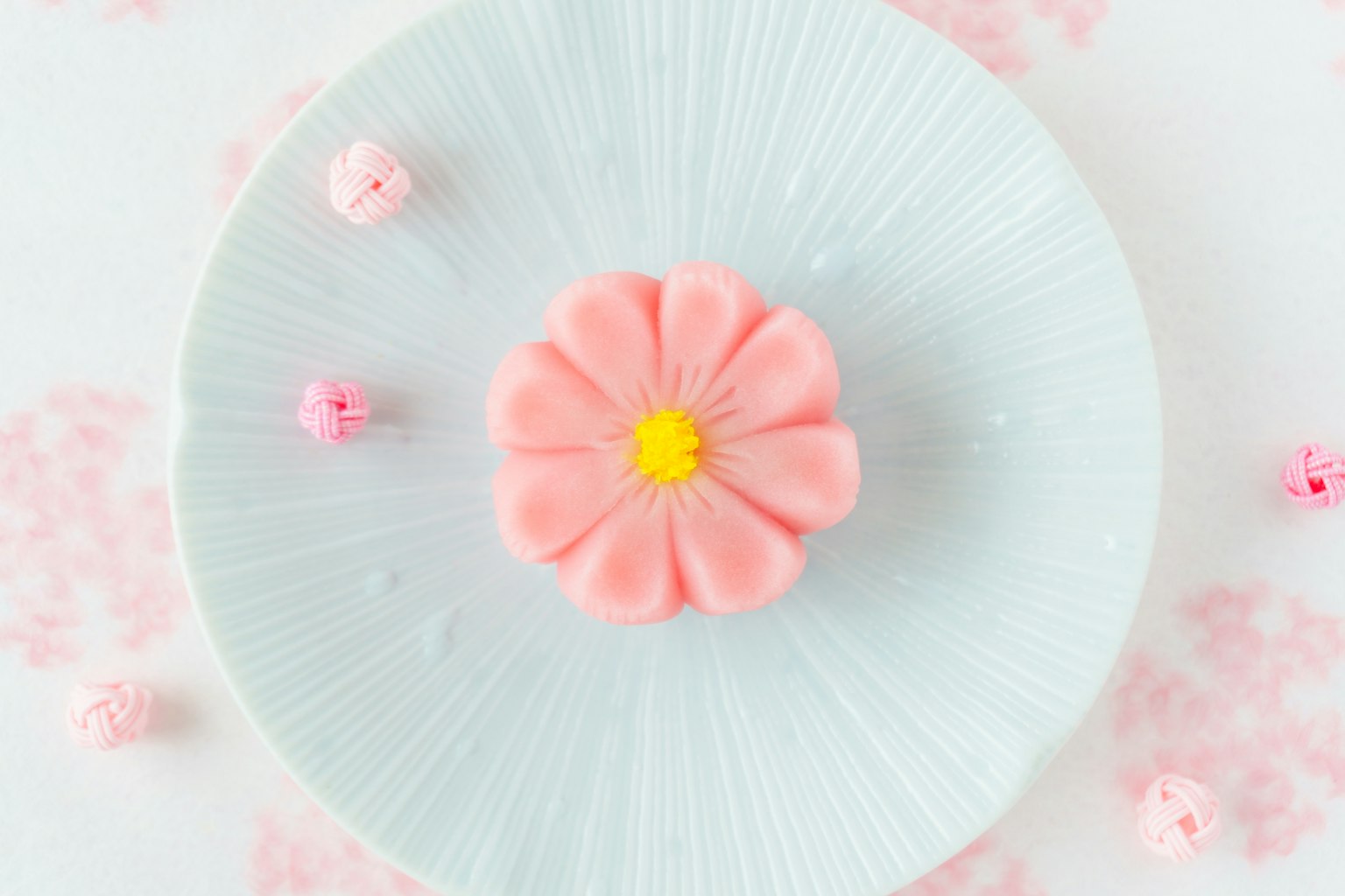 Un dulce japonés en forma de flor rosa sobre un plato azul claro con pequeñas decoraciones rosas