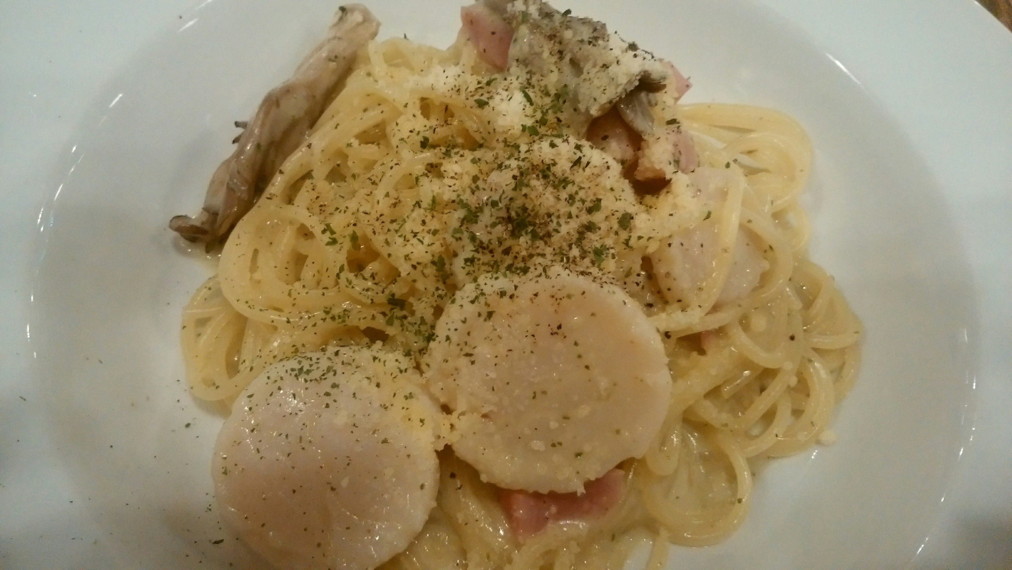 pasta con vieiras y bacon en un plato blanco