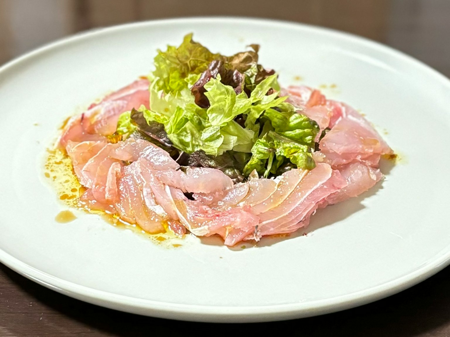 Pesce affettato finemente con insalata fresca su un piatto bianco