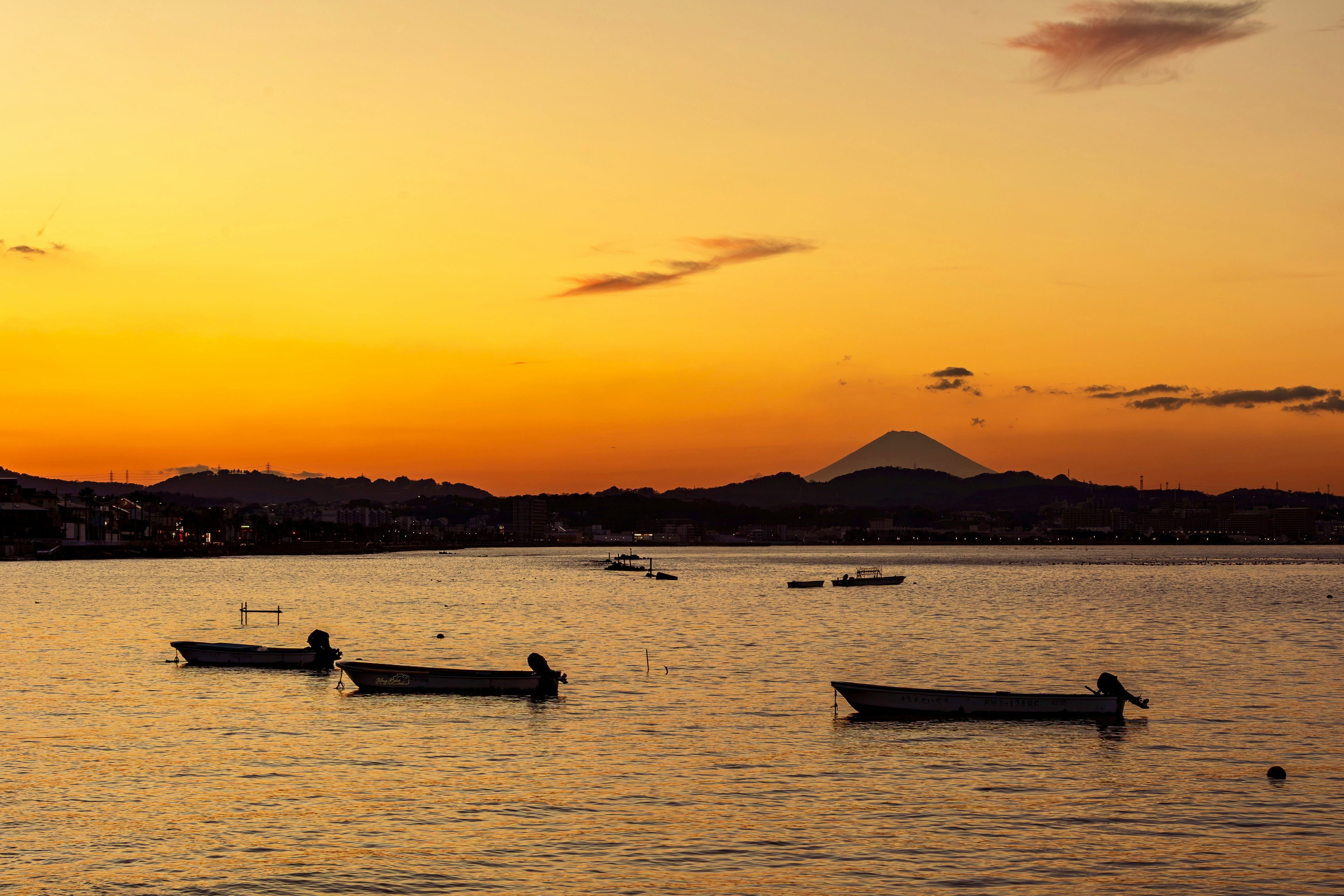 夕焼けの海辺で浮かぶ小舟と富士山のシルエット
