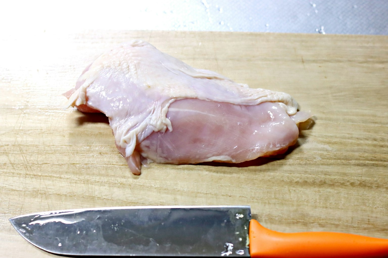 木砧板上的生鸡胸肉和橙色刀具