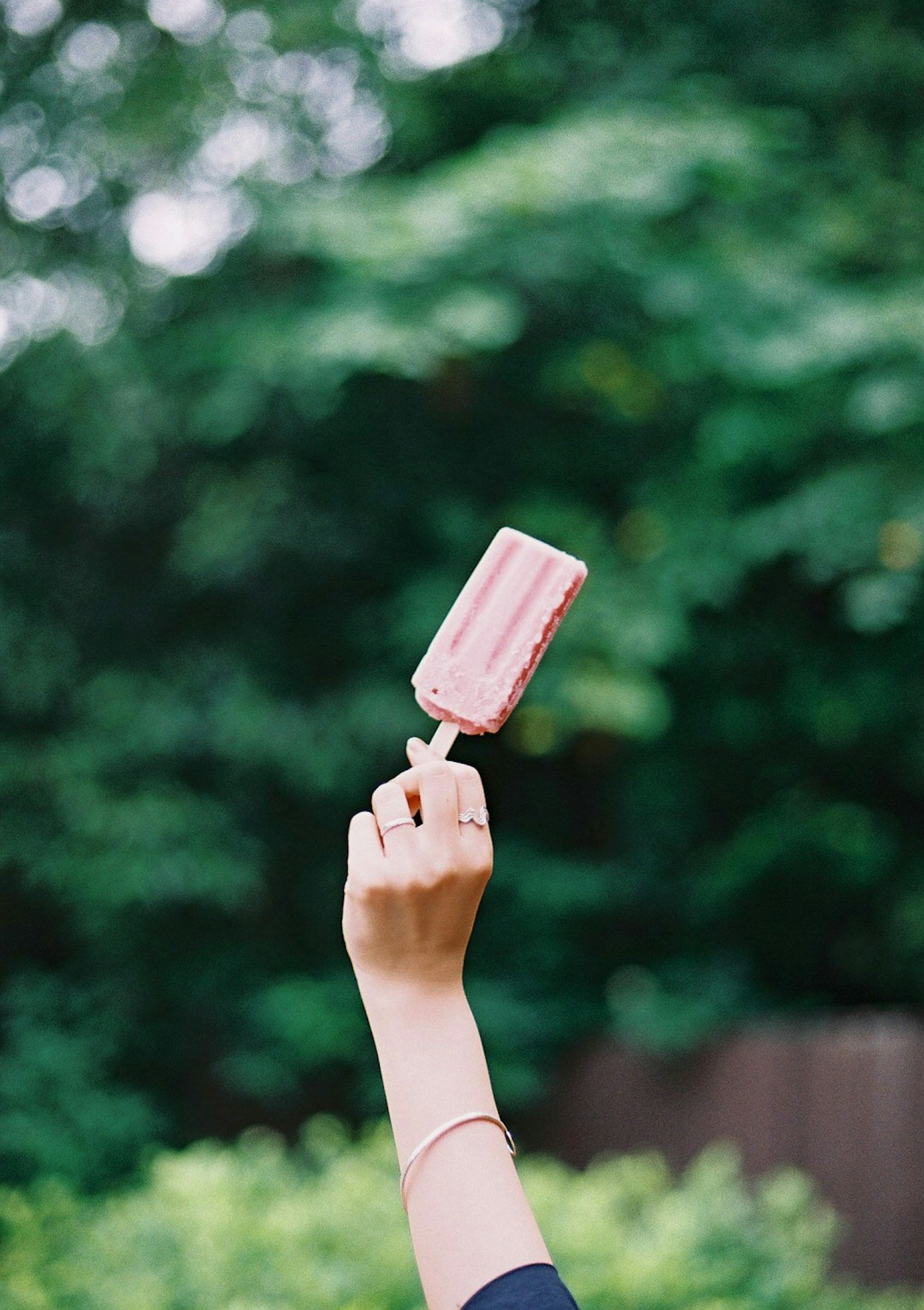 Hand, die ein rosa Eis am Stiel vor grünem Hintergrund hält