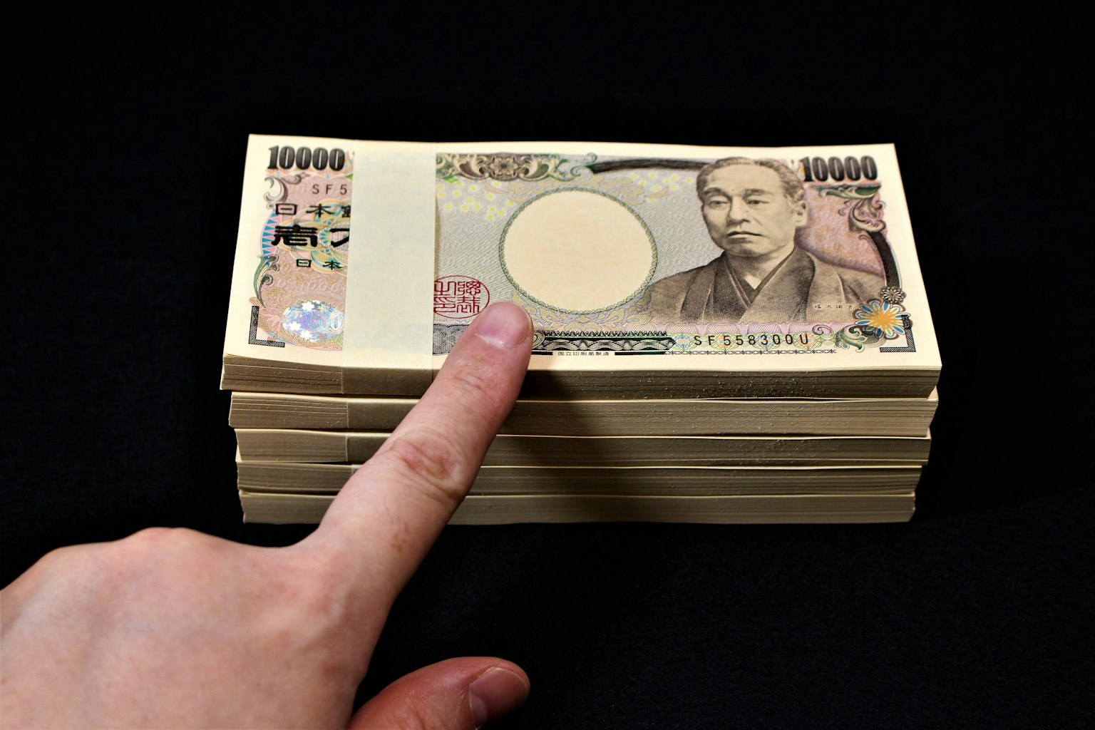 一疊日本10000日圓鈔票上放著一根手指